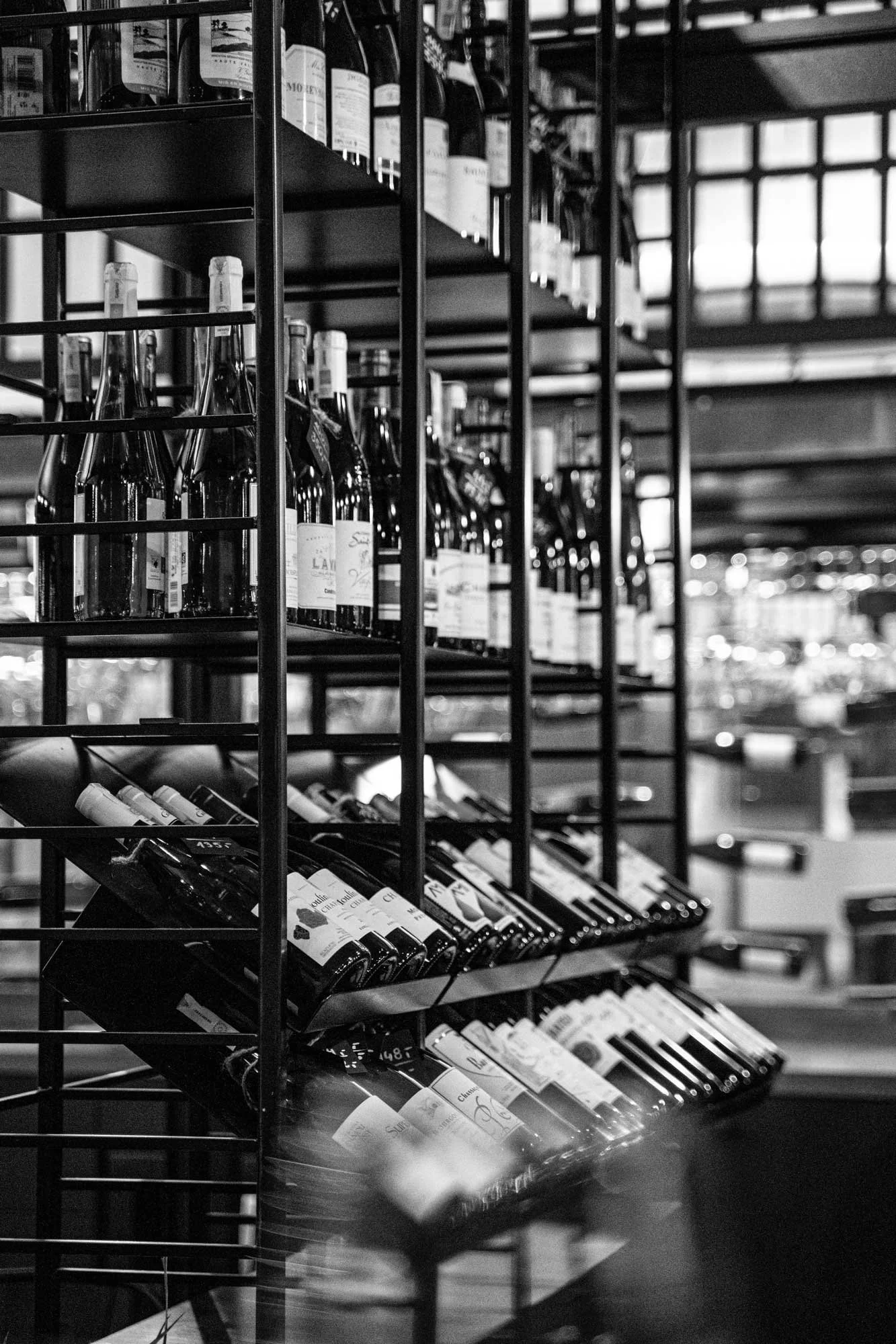 Black and white photo of a wine display shelf with bottles of wine arranged on angled racks in a store or restaurant.