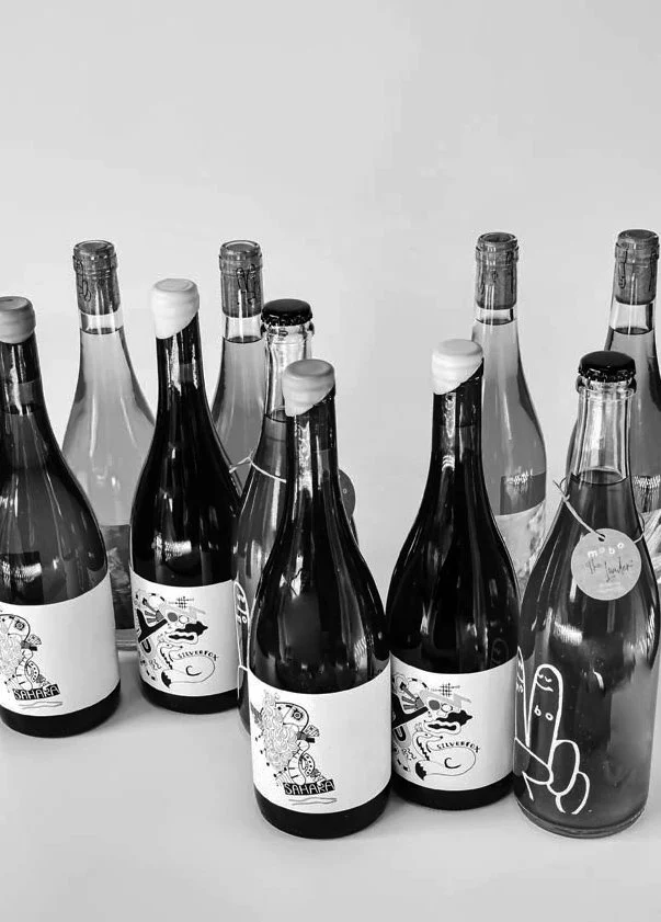 Nine glass bottles arranged on a table, each with unique illustrated labels and sealed with different caps.