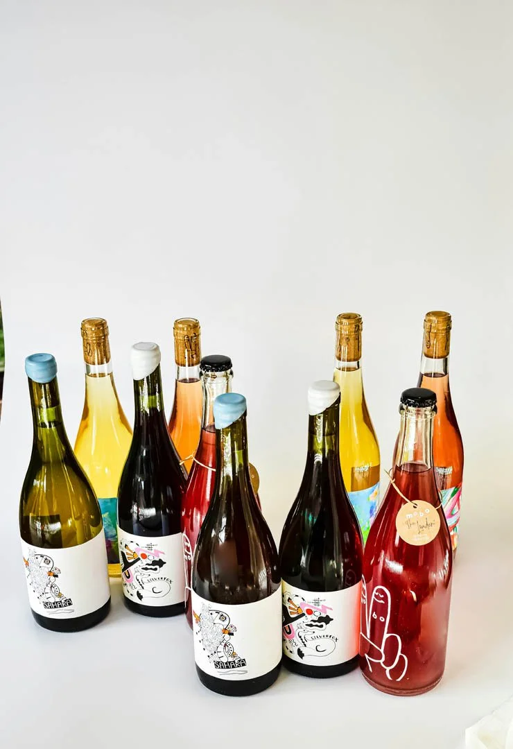 A collection of colorful bottles, some with artistic labels, arranged on a plain white surface against a white background.
