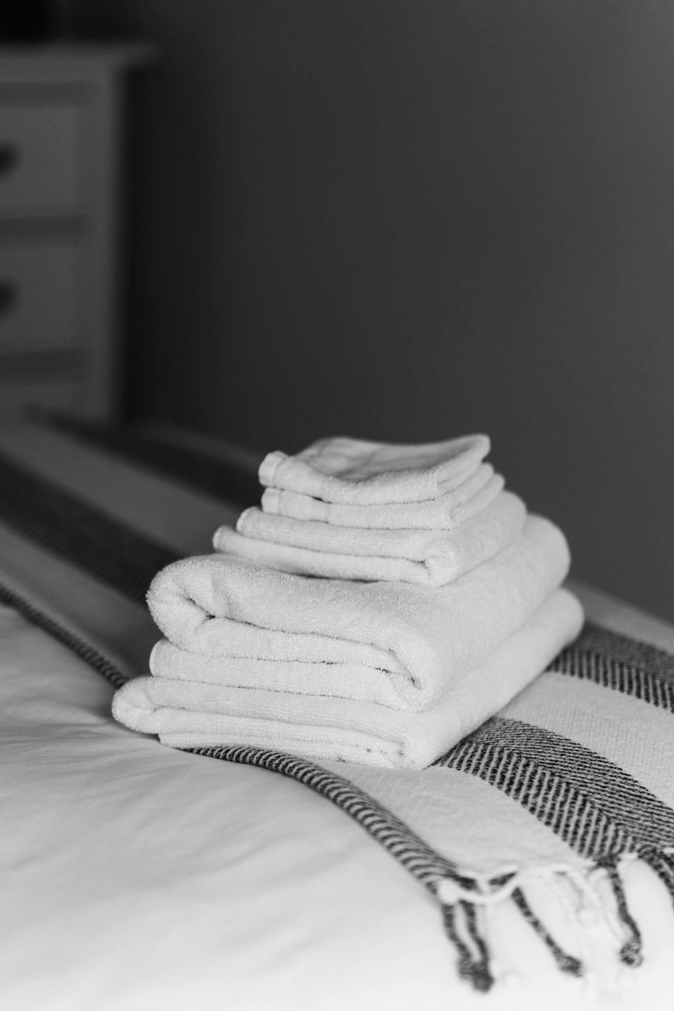A stack of folded white towels and washcloths placed on a bed with a striped blanket in a bedroom setting.