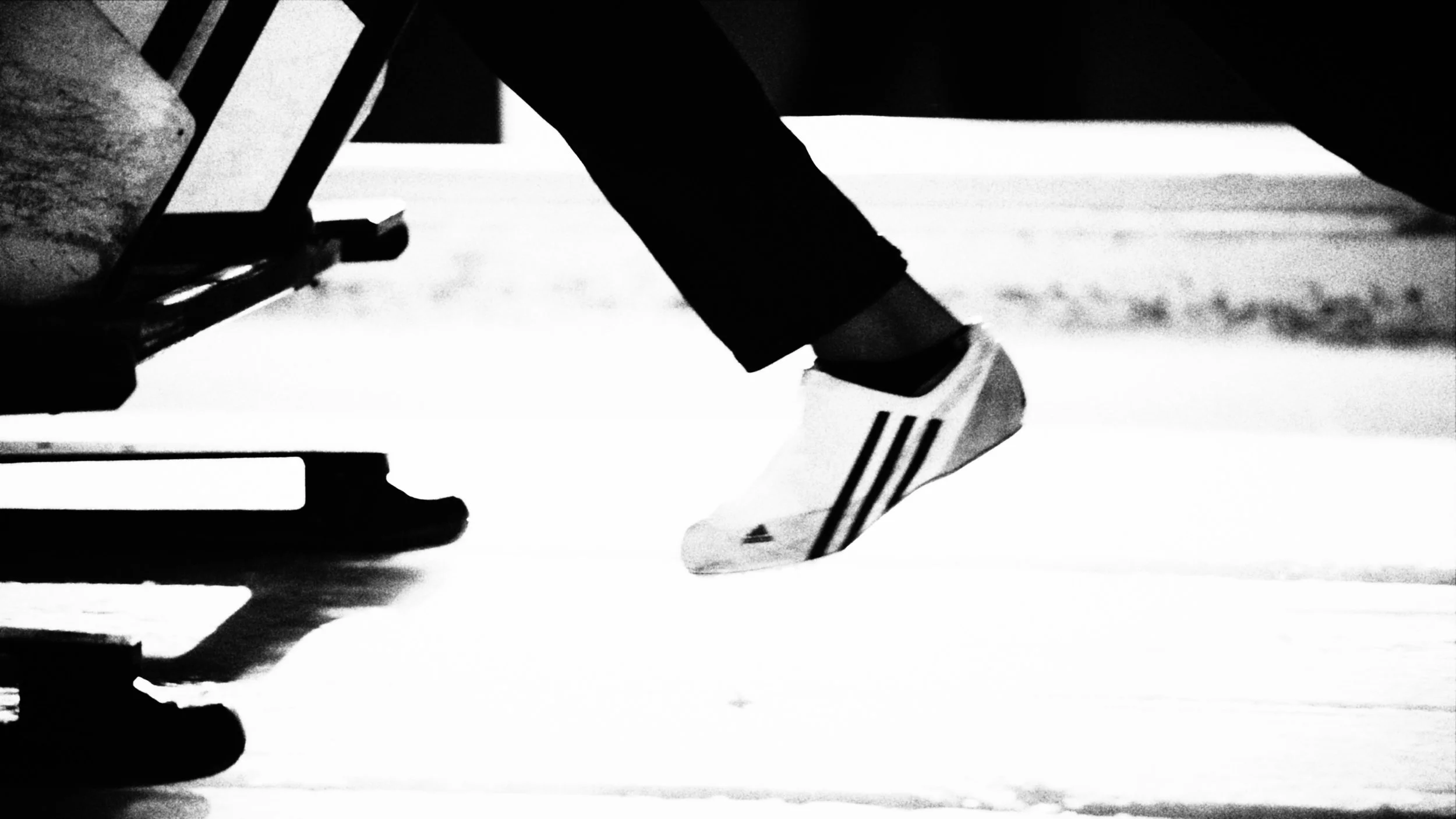 Close-up of a person's foot in athletic shoe on ice, next to a sledge, with the ice rink surface visible in the background.