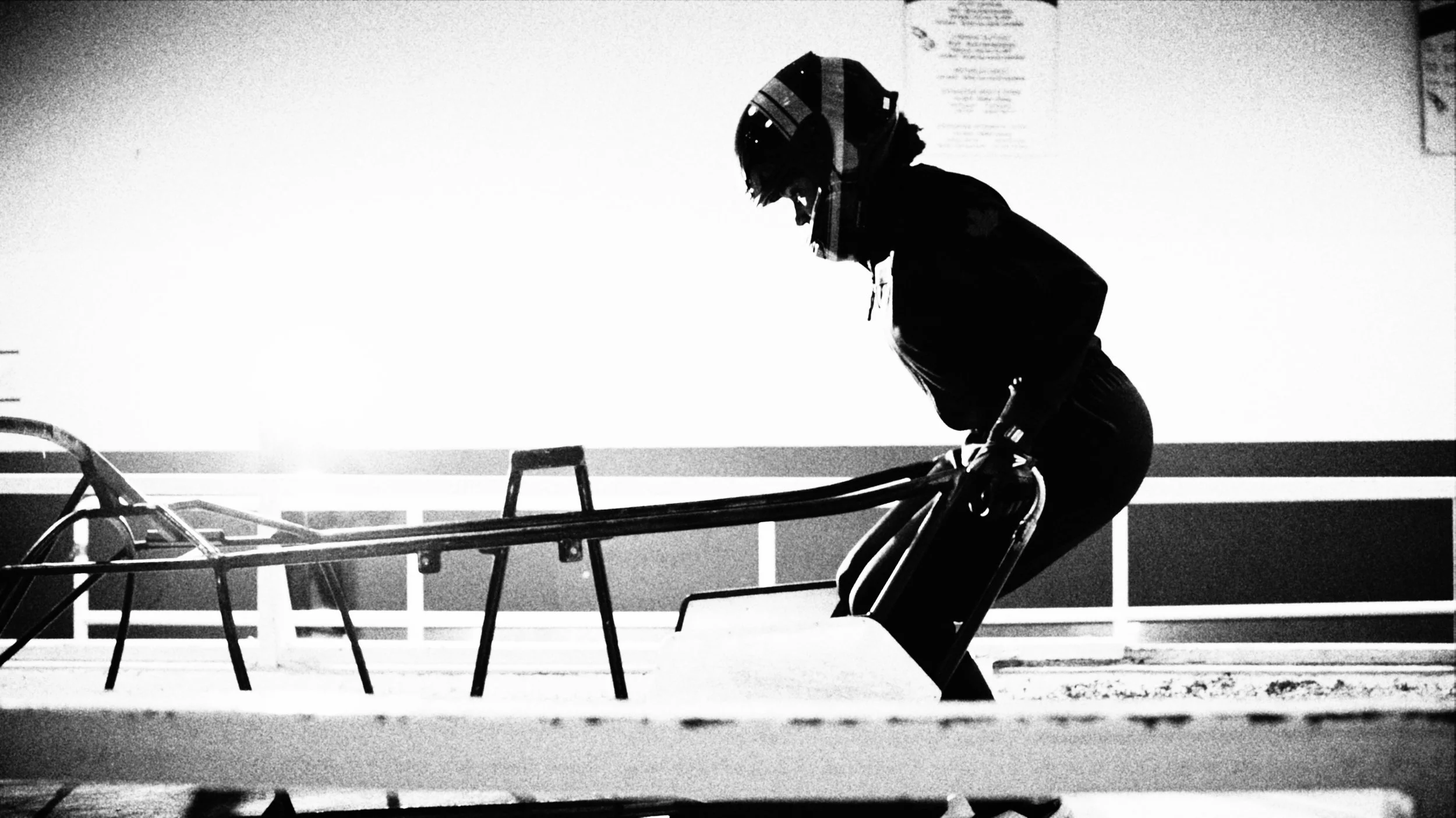 A person wearing a helmet and dark clothing leaning on a training bobsled at the start of a track