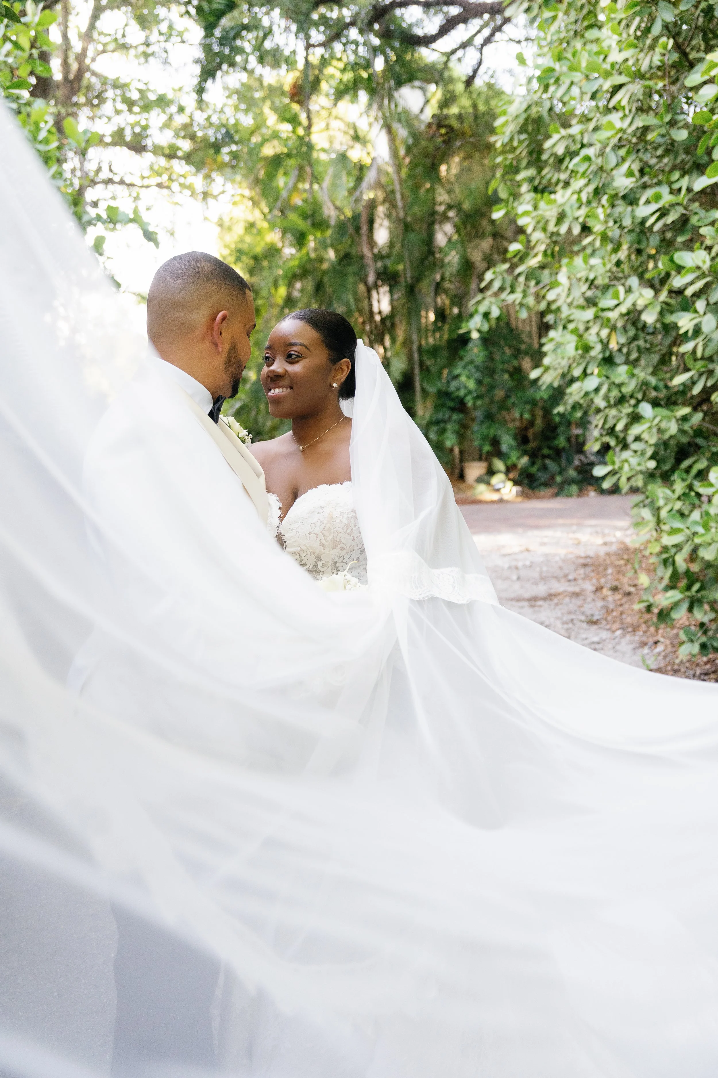 A bride and groom sharing an intimate moment outdoors, surrounded by green foliage, on their wedding day.