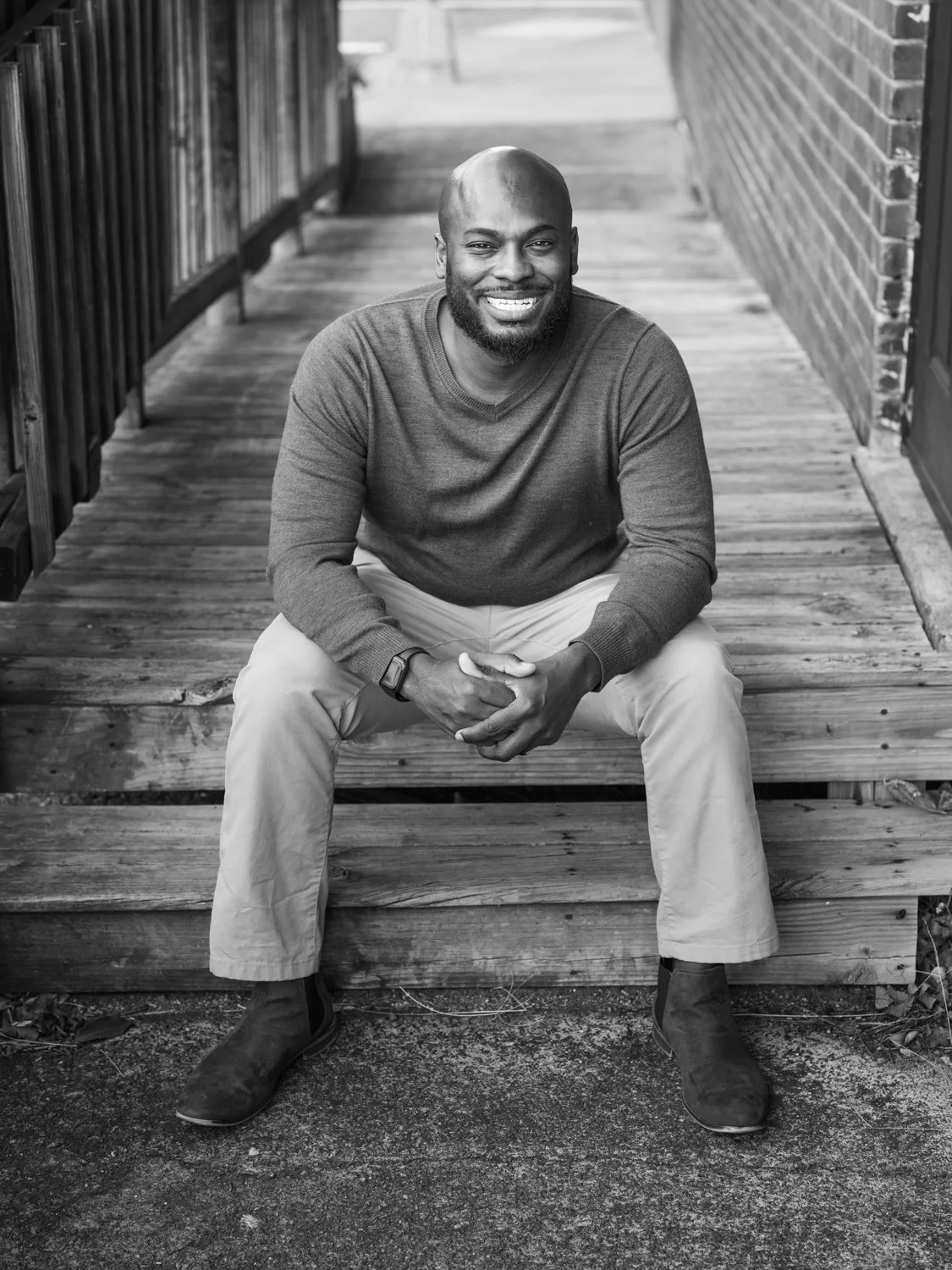 A smiling man sitting on wooden stairs outside.