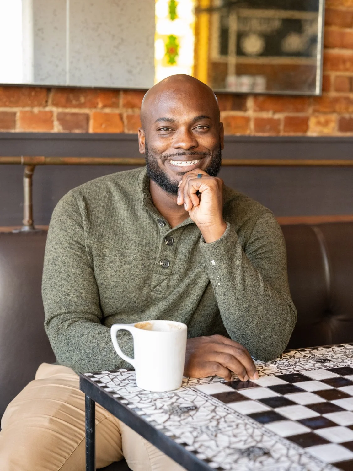 A smiling man sits at a table in a cafe.