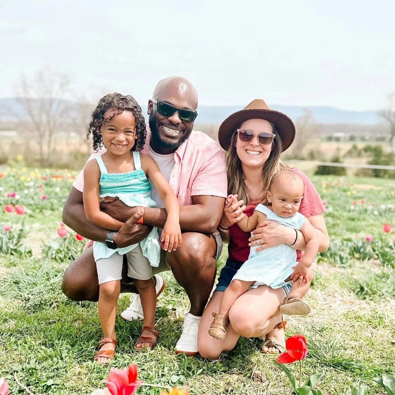 Family of four outdoors in a field of tulips, smiling and posing for the camera.