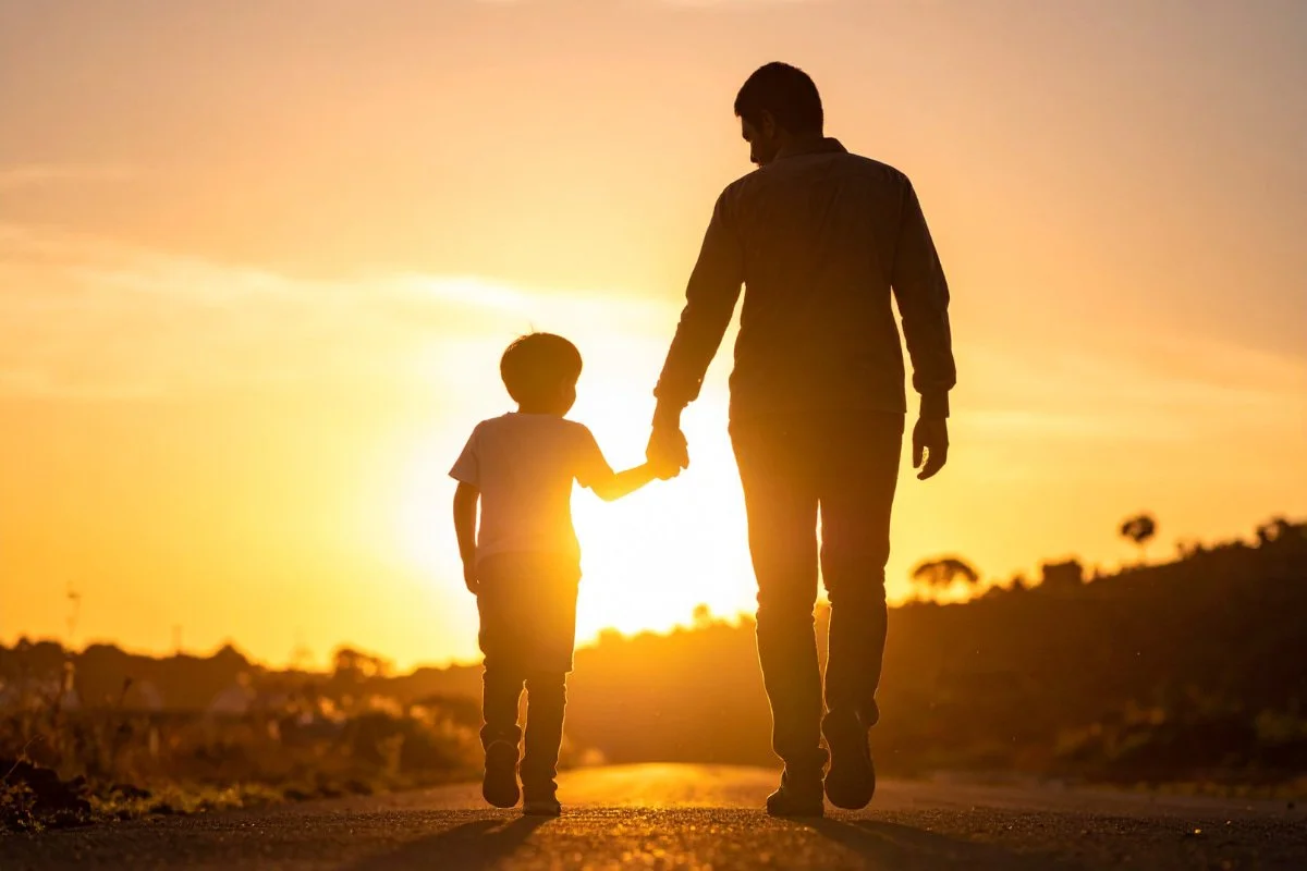 Silhouette of a father and son walking hand in hand on a road during sunset