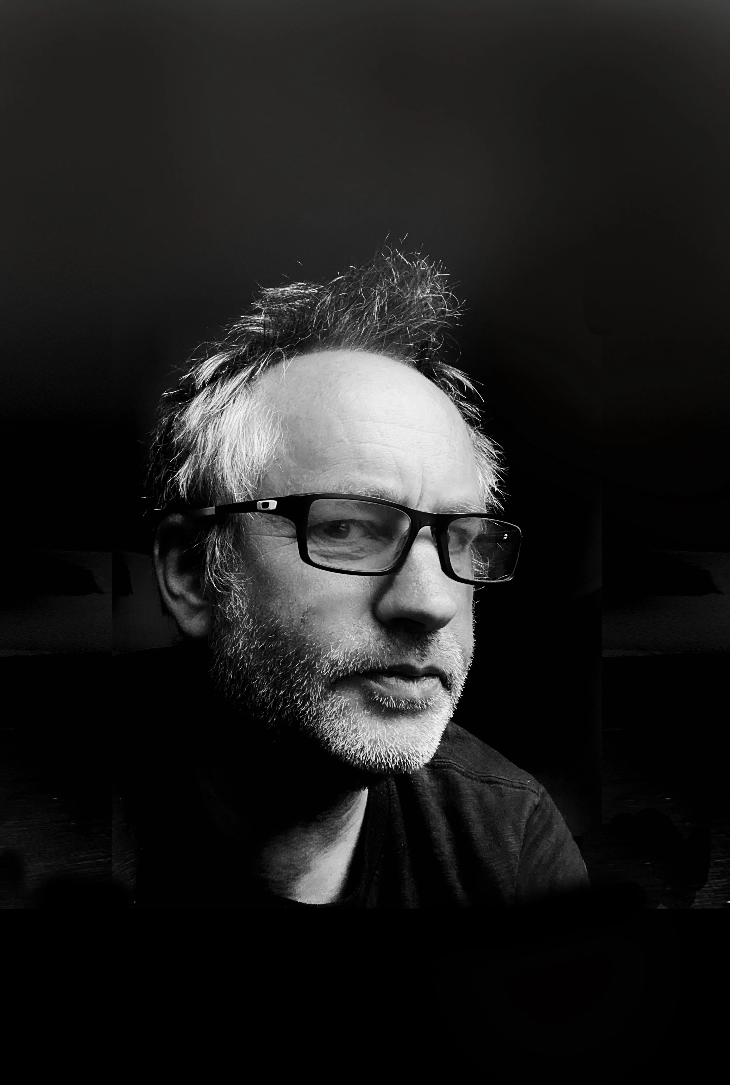 Black and white portrait of a middle-aged man with glasses, a beard, and messy hair, looking slightly to the side.