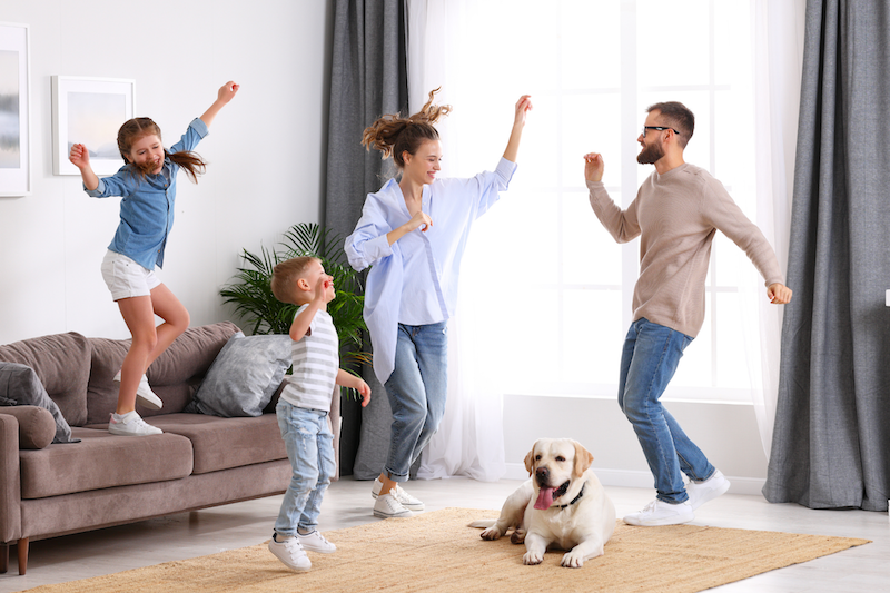 Family dancing and playing with a dog in living room.