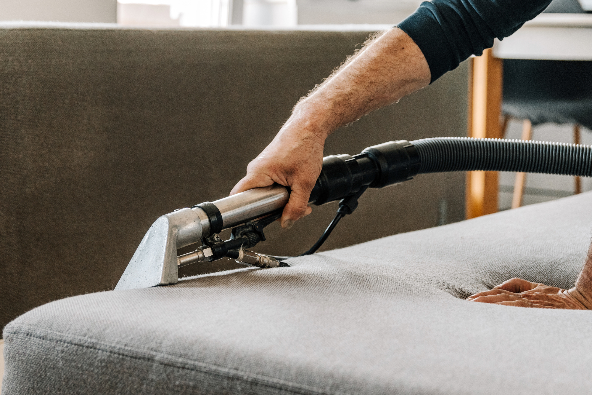 Person using a vacuum cleaner to clean a beige couch.