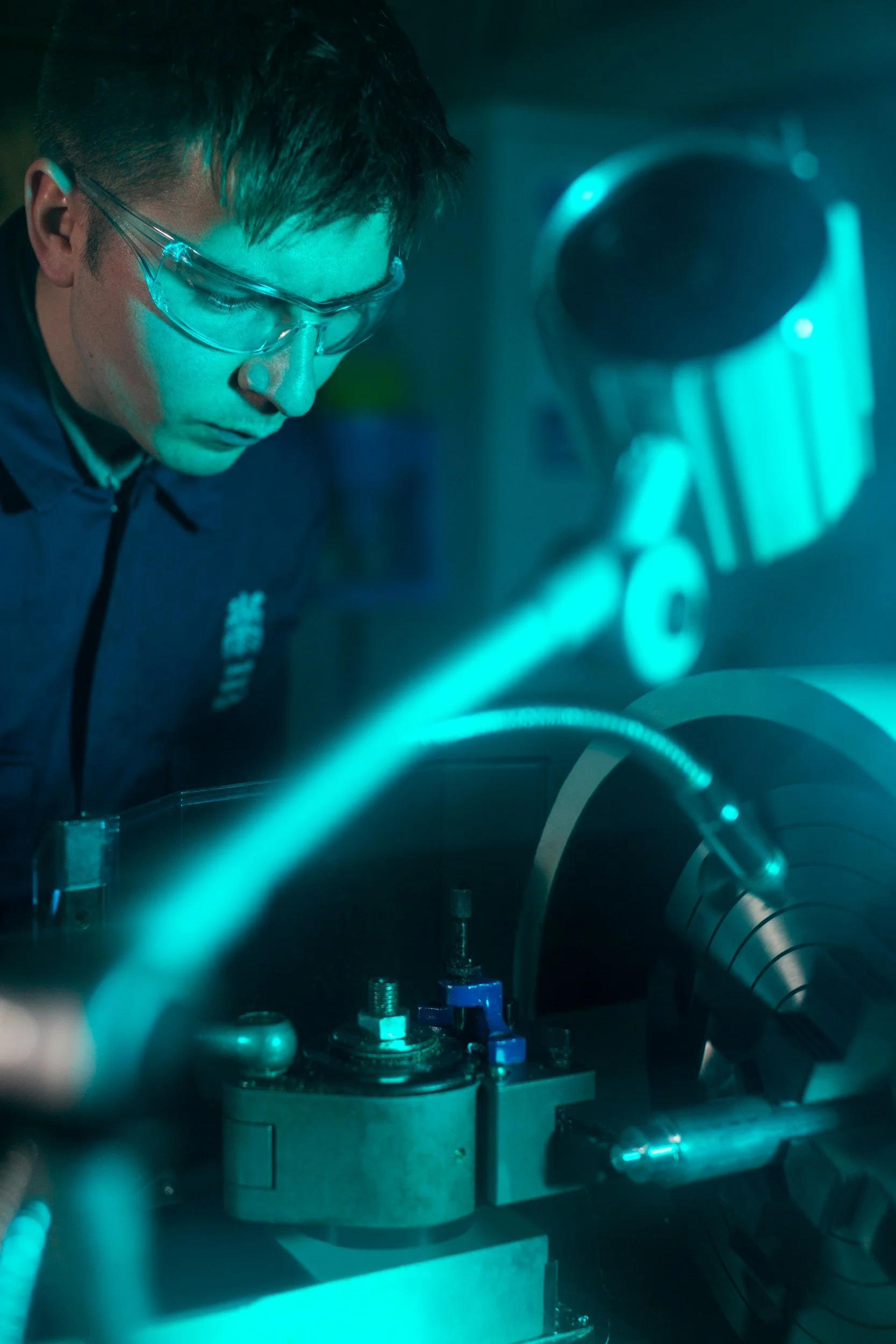 A scientist wearing safety glasses working with a glowing laser beam in a laboratory.