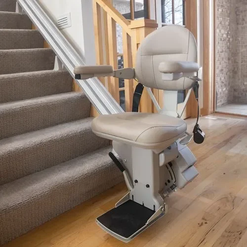 A stairlift chair installed on a staircase next to a wall in a house interior, with hardwood flooring and a sliding door in the background.