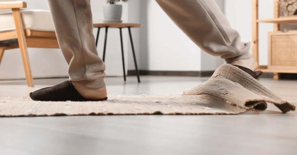 Person stepping on a rolled-up rug inside a room with wooden furniture.