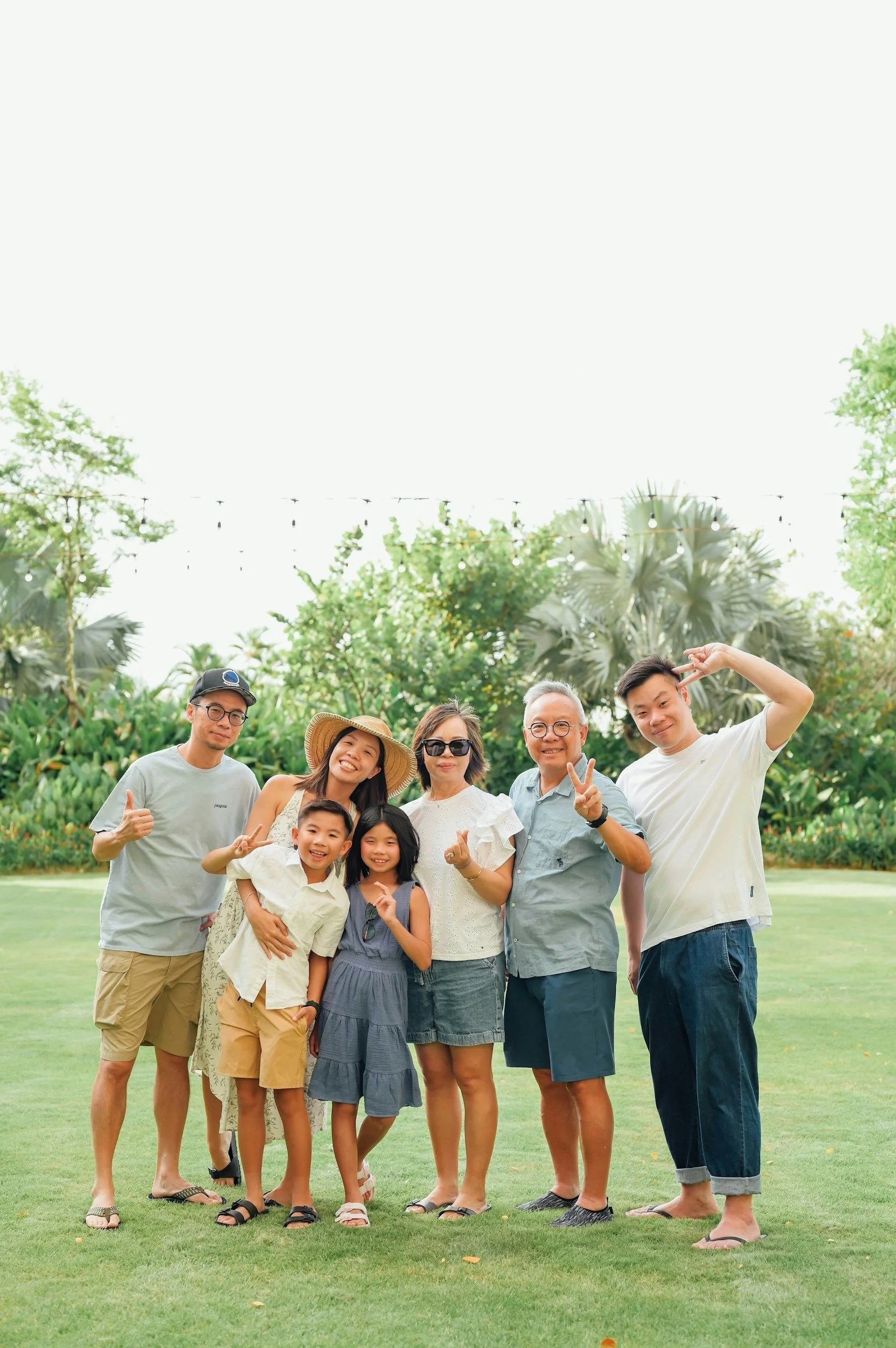 Group of people outdoors on a grassy lawn, smiling and posing for a photo with trees and string lights in the background.