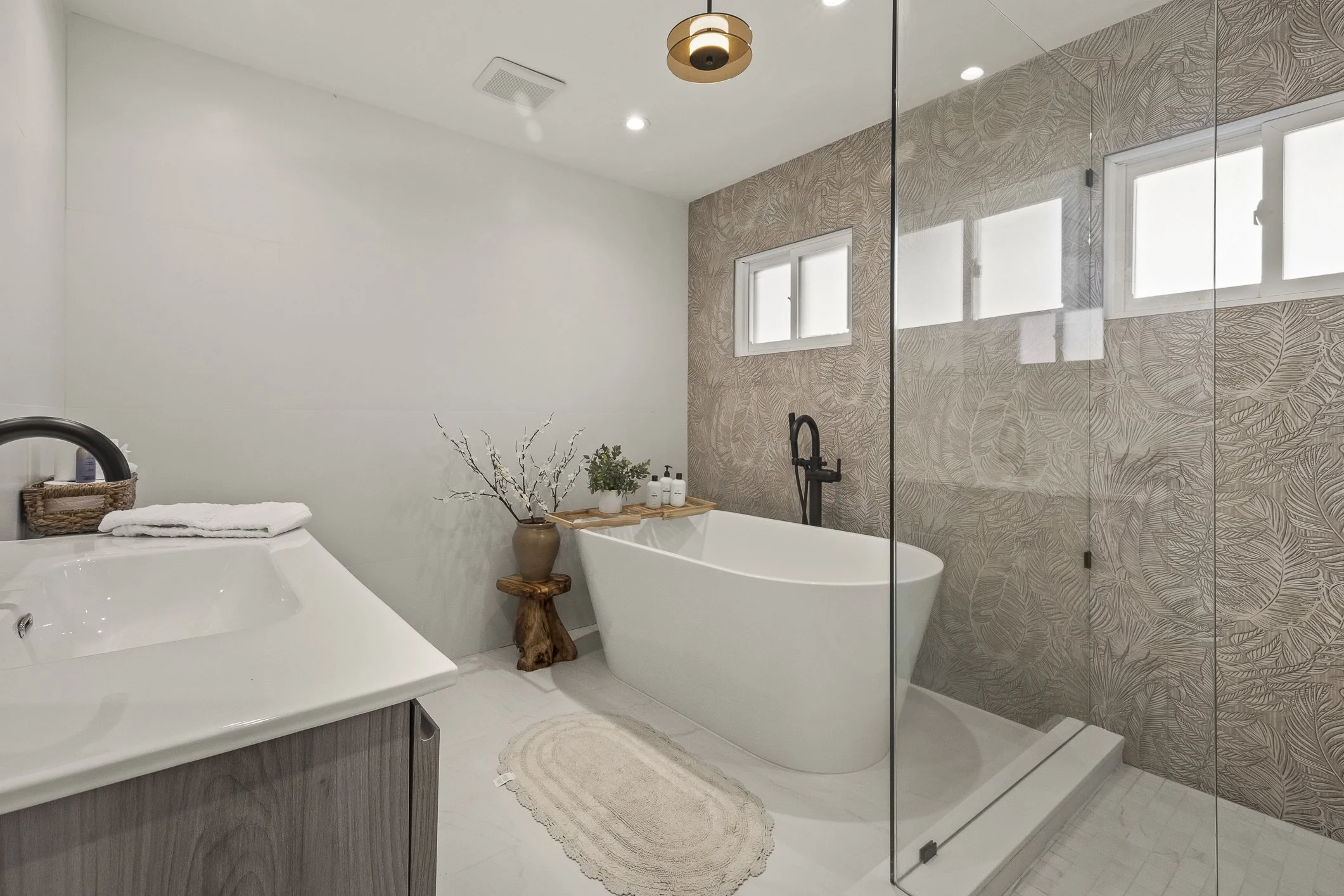 Modern bathroom with white bathtub, vanity, and a walk-in shower with glass door; neutral tones, natural wood accents, and decorative wall design.