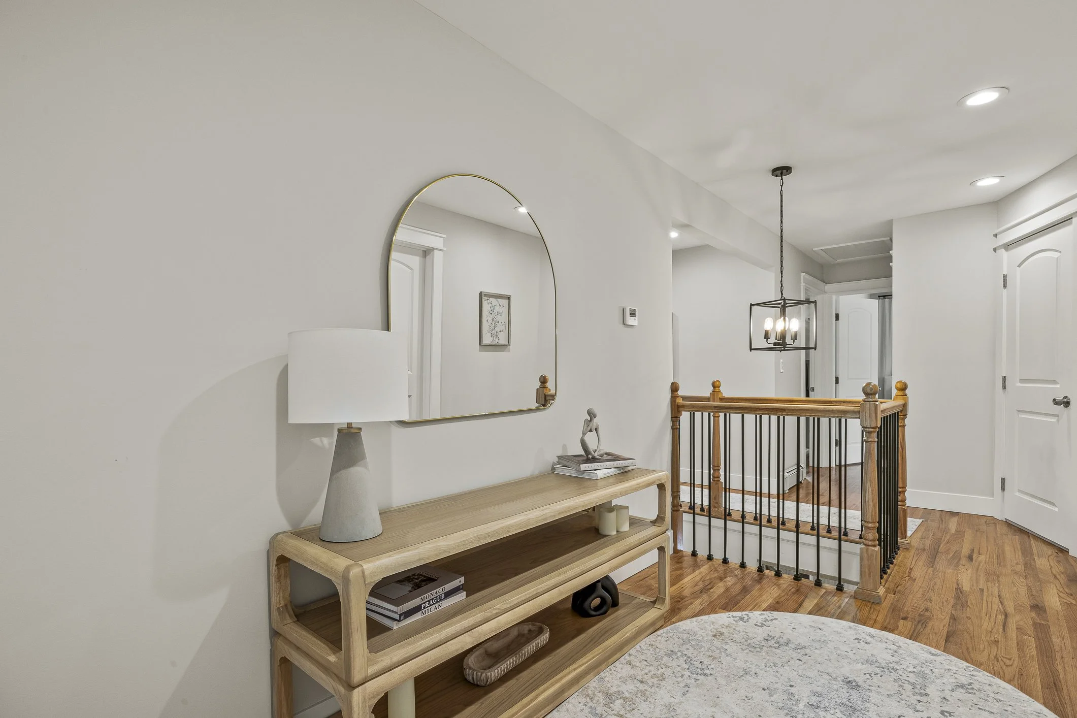 Interior view of a modern home entryway with a wooden bench, decorative items, and a mirror on a white wall.