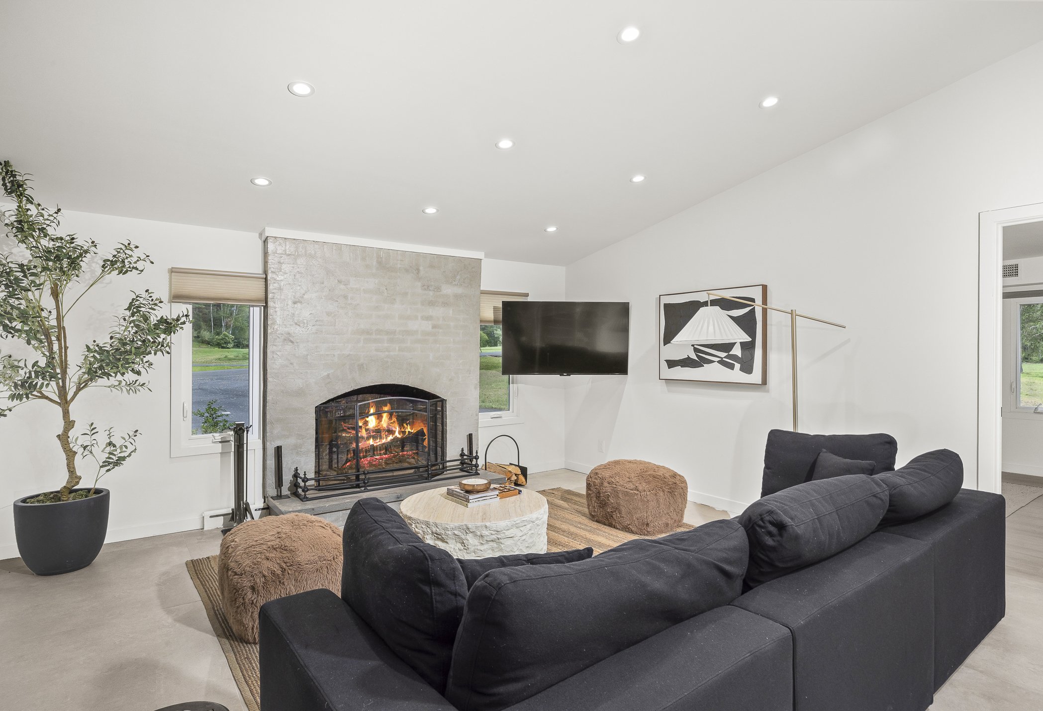 Modern living room with white walls, a fireplace, a black sofa, a potted plant, a wall-mounted TV, and abstract wall art.