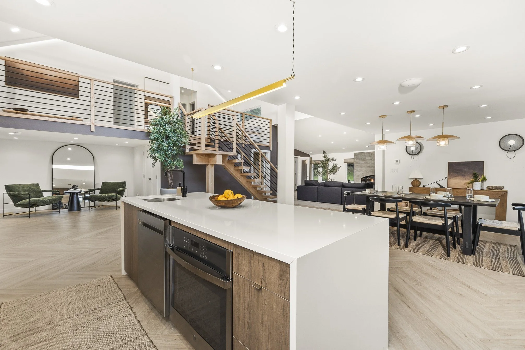 Open-concept living space with a kitchen island, dining area, living room, staircase, and upstairs balcony in a modern home