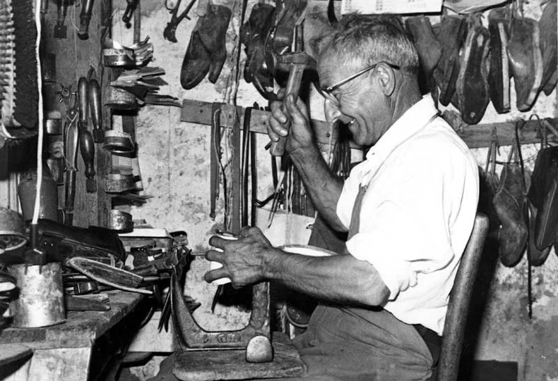 Calzolaio napoletano intento a lavorare nella sua bottega tradizionale. L’immagine richiama la figura dello “scarparo”, da cui prende nome lo scarpariello, piatto nato tra artigiani e botteghe popolari.