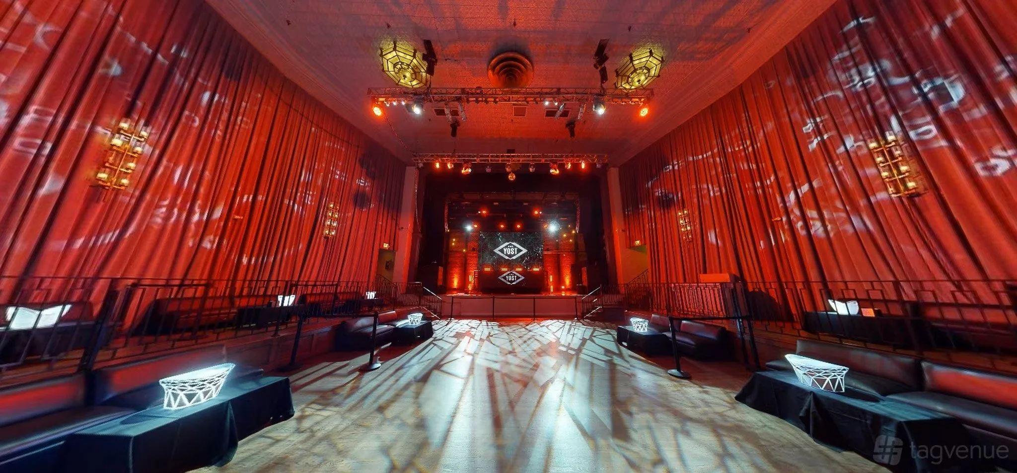 Empty event venue with a large stage, red curtains, and decorative lighting, ready for a performance or event.