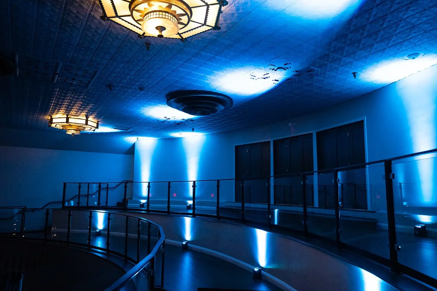 Interior of a dimly lit building with blue lighting, an escalator, and ceiling lights.