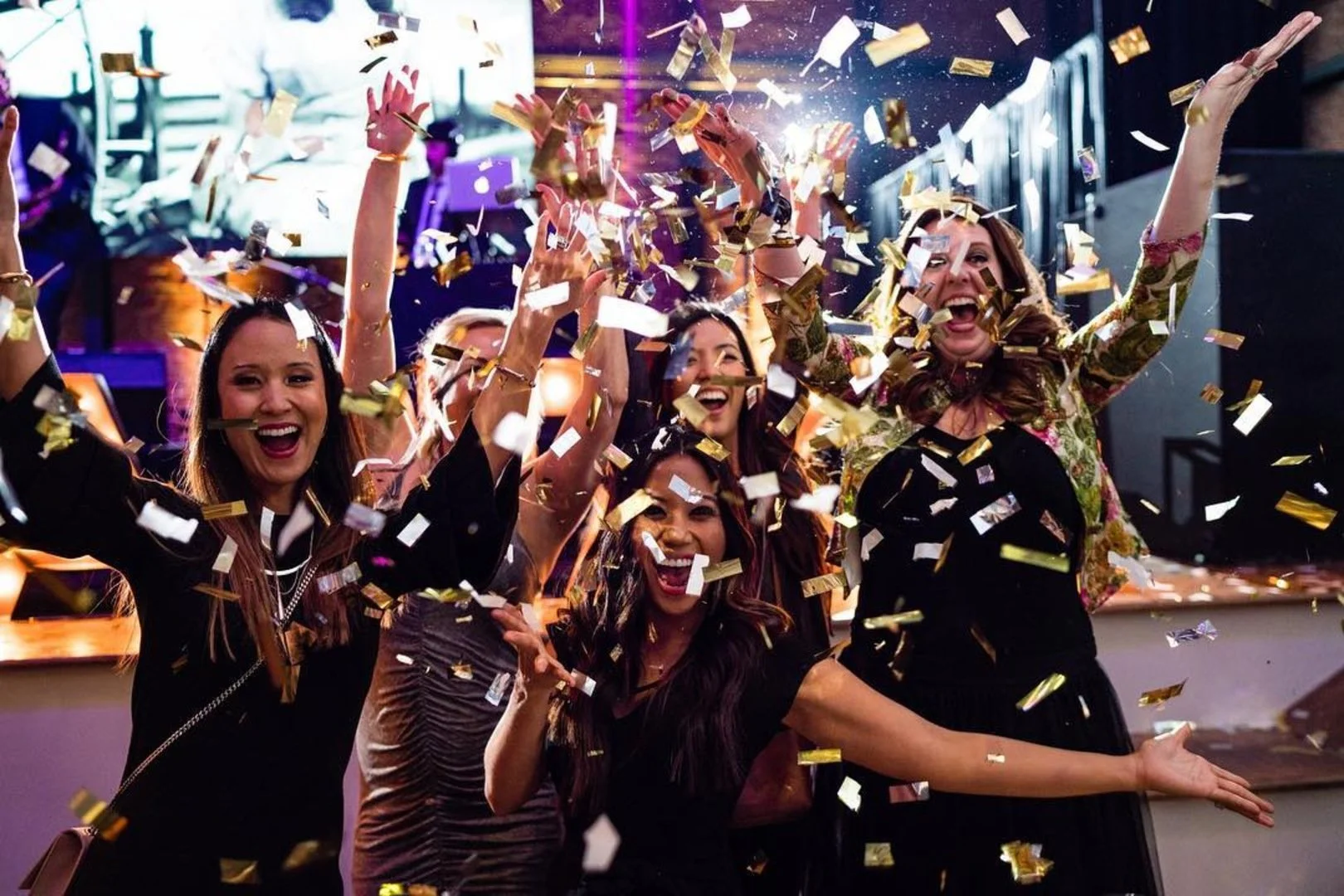 Group of women celebrating with confetti in a festive setting, smiling and raising their hands.