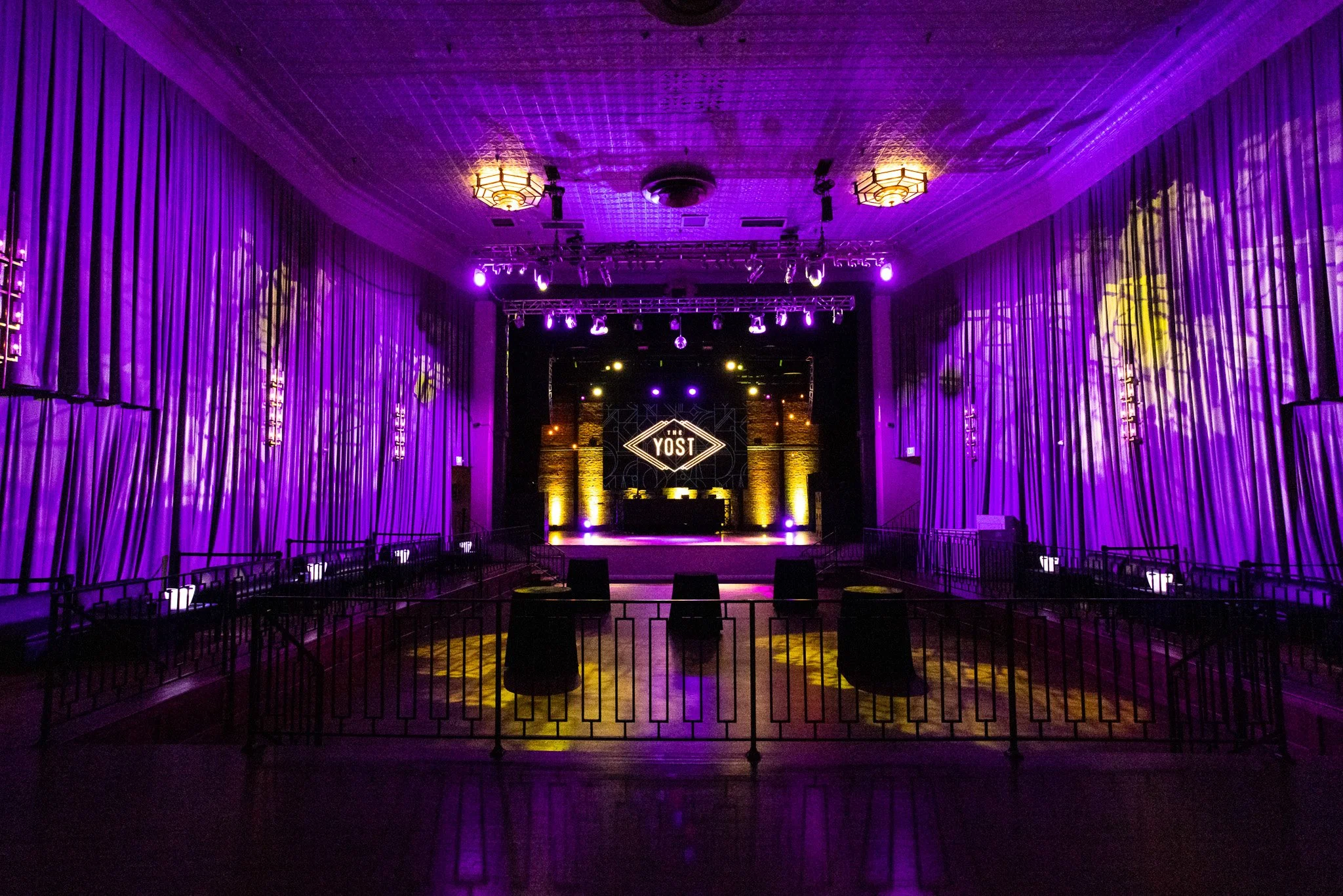 Empty theater stage with purple lighting, curtains, and a sign that reads 'The Yost' at the back.
