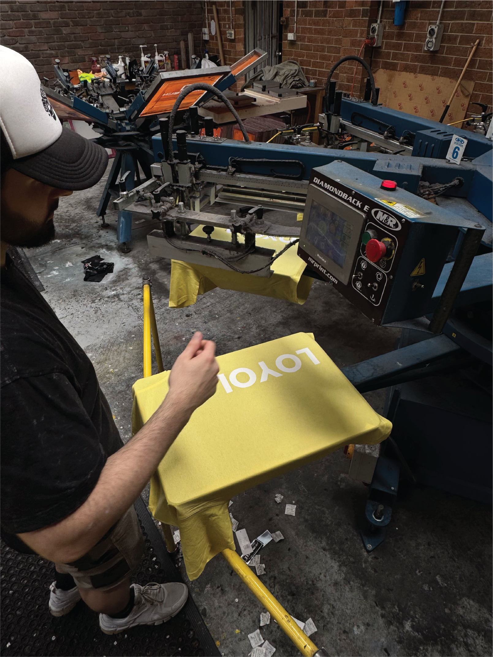 A person operating a screen printing press to create yellow tote bags with white letters.