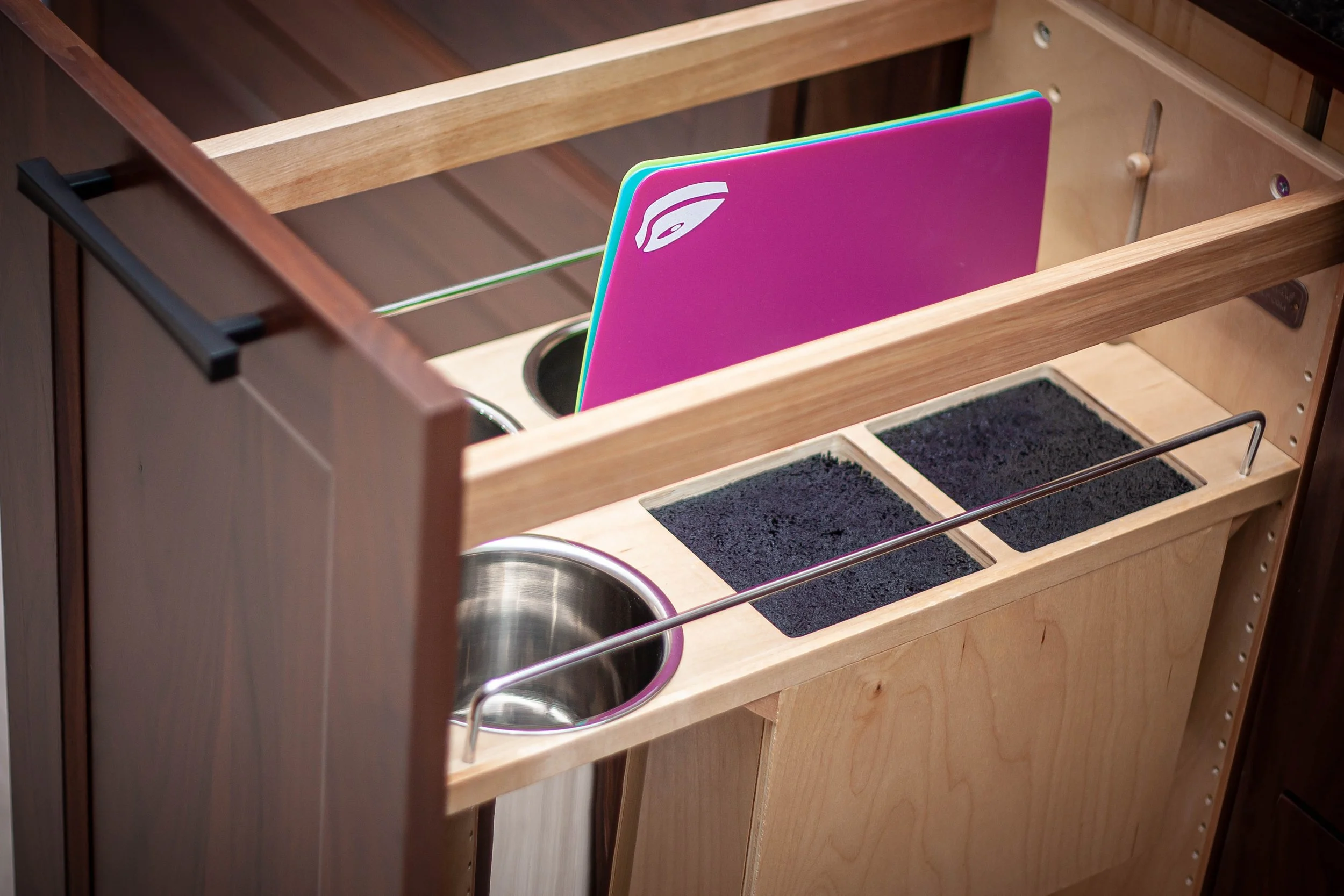 Custom pull-out wood cabinet organizer displaying built-in metal canisters and color-coded cutting board storage.