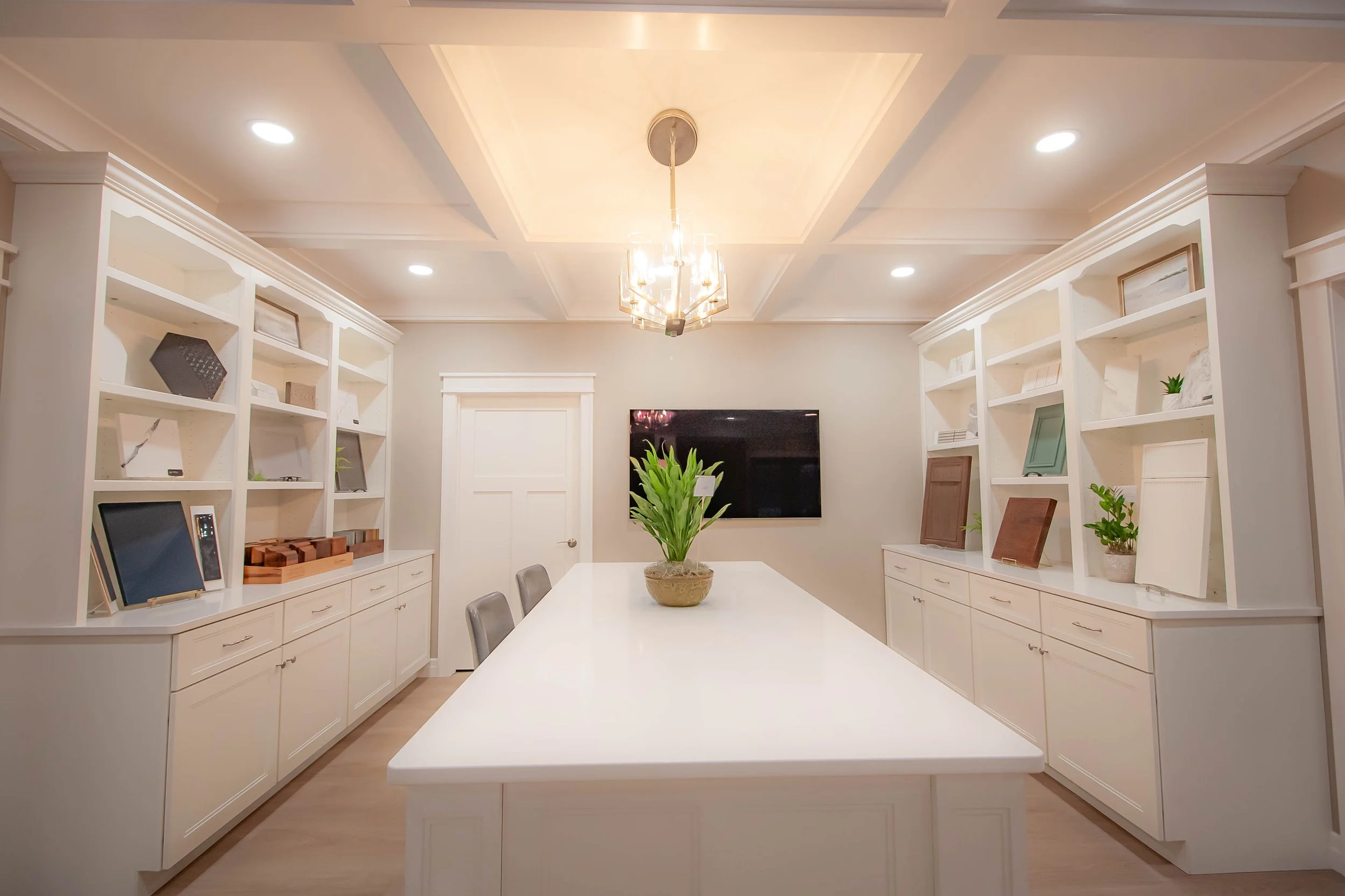 Bright white custom kitchen island display featuring classic white inset cabinetry, matching paneled pillars, and a coffered ceiling.