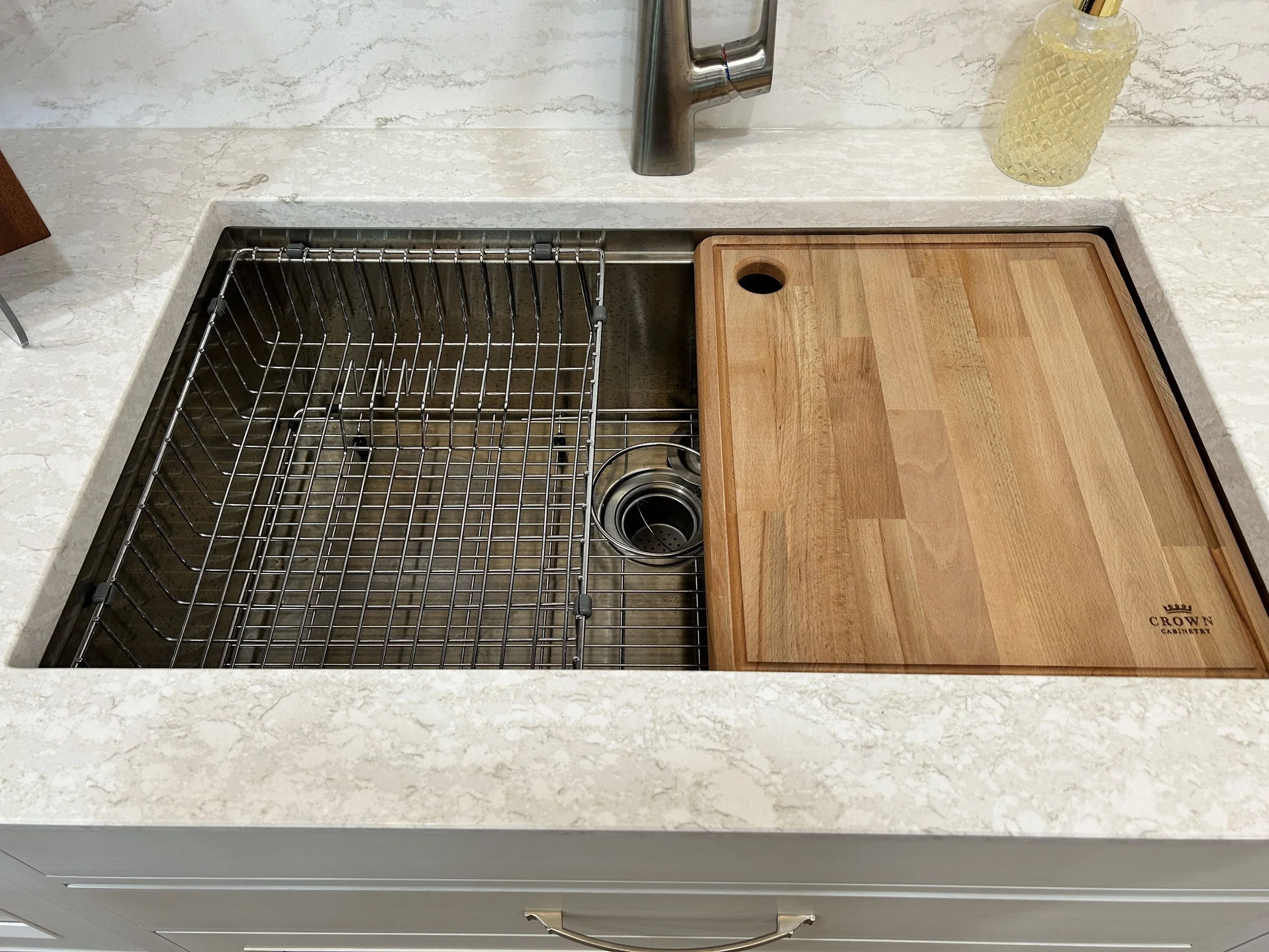 Close-up of a premium kitchen workstation sink featuring an integrated wood cutting board and stainless steel grid insert.