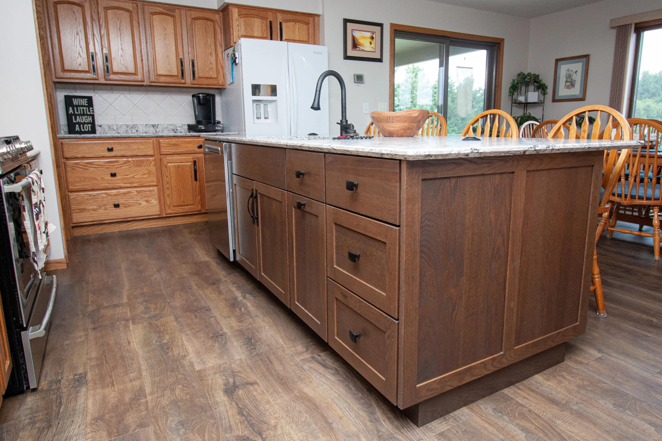 Kitchen remodel featuring honey oak perimeter cabinets, a dark stained wood island with matte black knobs and pulls, a white patterned granite countertop, and a black goose-neck faucet