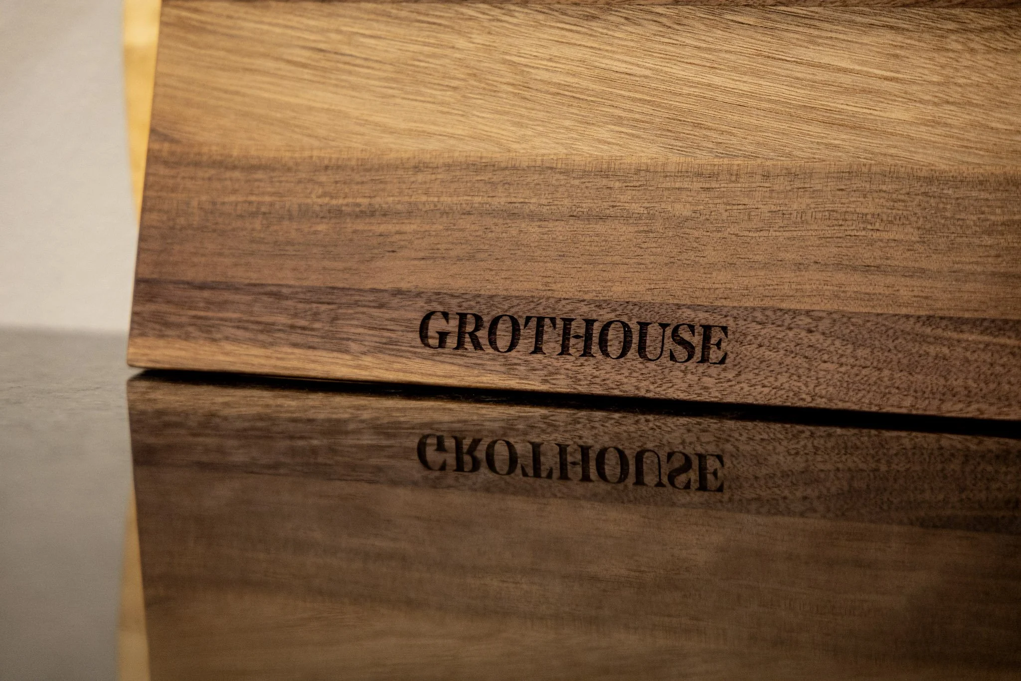 Close-up of a wooden box with the word "GROTHOUSE" engraved on it, reflected on a shiny surface.