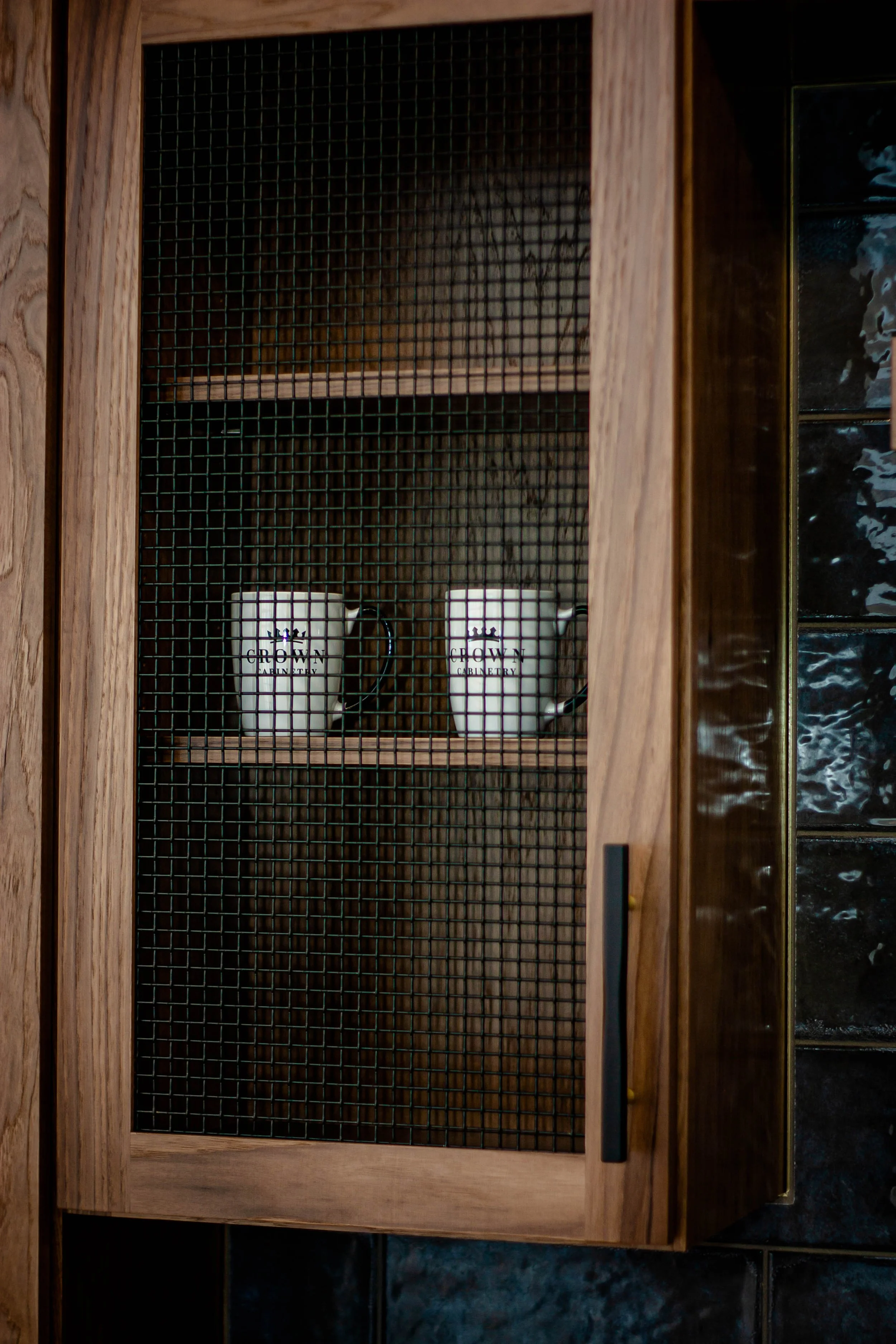 Close-up of a custom wood cabinet door featuring a decorative dark wire mesh insert and a ceramic mug display inside.