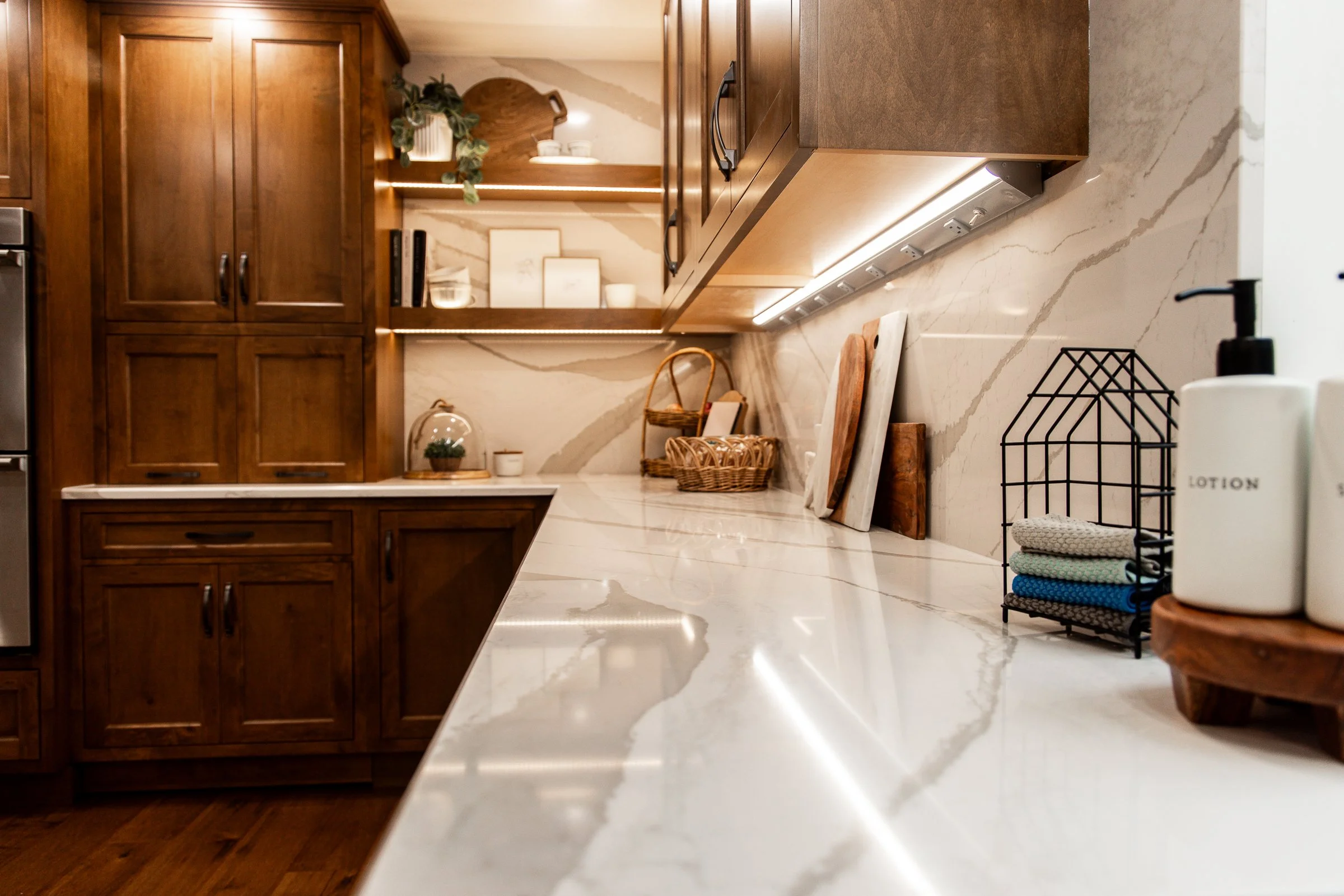 Custom warm wood cabinetry prep station with a continuous veining quartz countertop and seamless backsplash featuring under-cabinet lighting