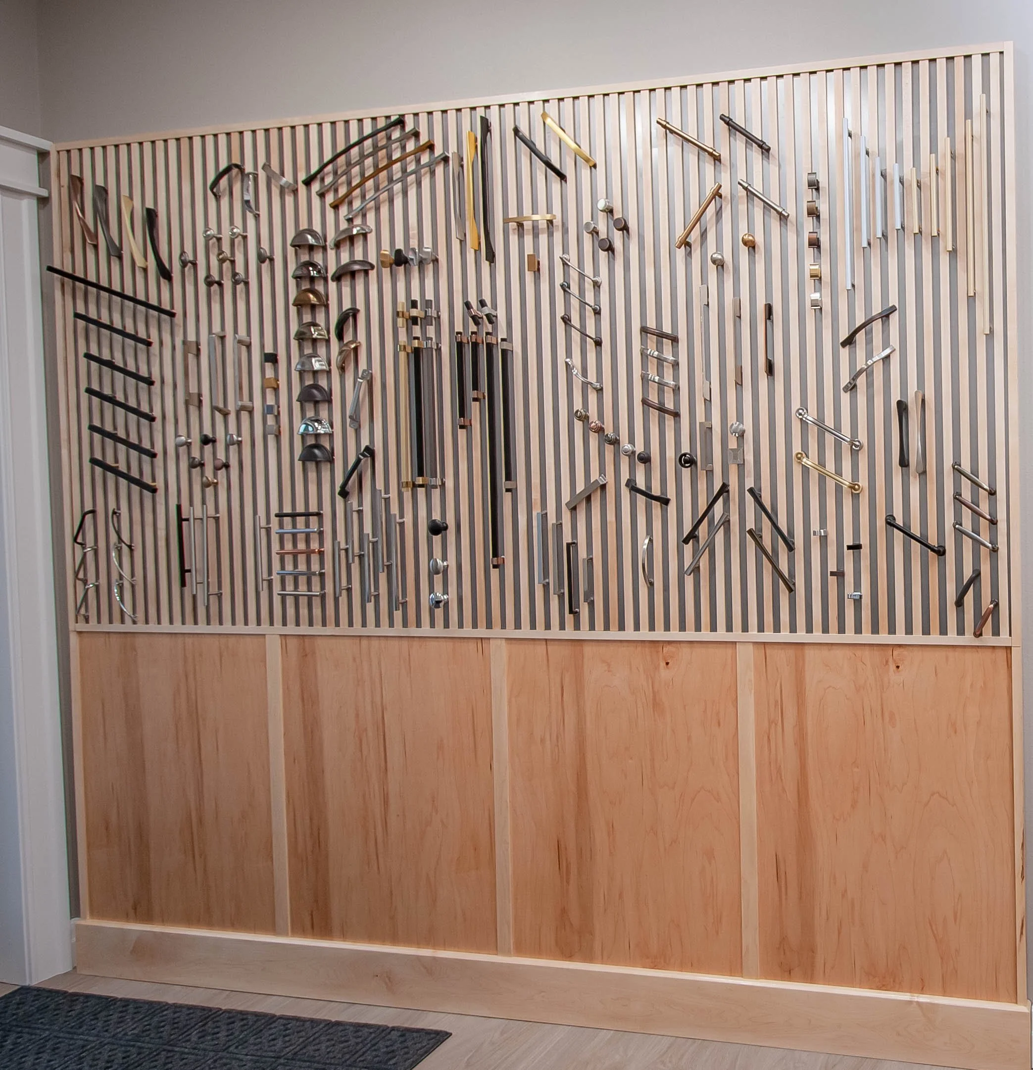 A comprehensive showroom display wall showcasing various styles of modern cabinet knobs, pulls, and designer hardware on a wood slatted background.