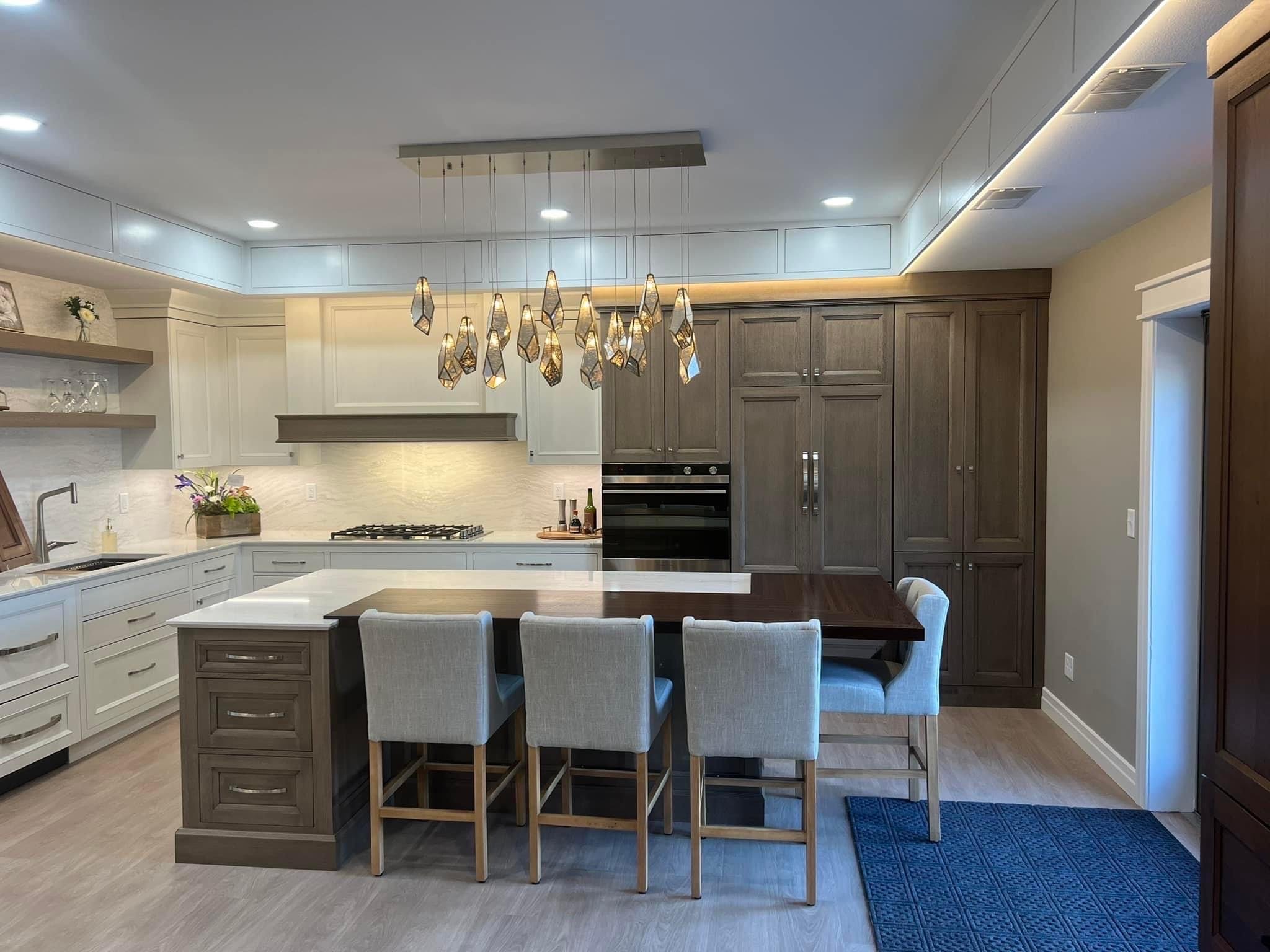 Luxury showroom kitchen display with a warm gray center island, modern glass chandelier, and rich floor-to-ceiling dark walnut perimeter cabinets.
