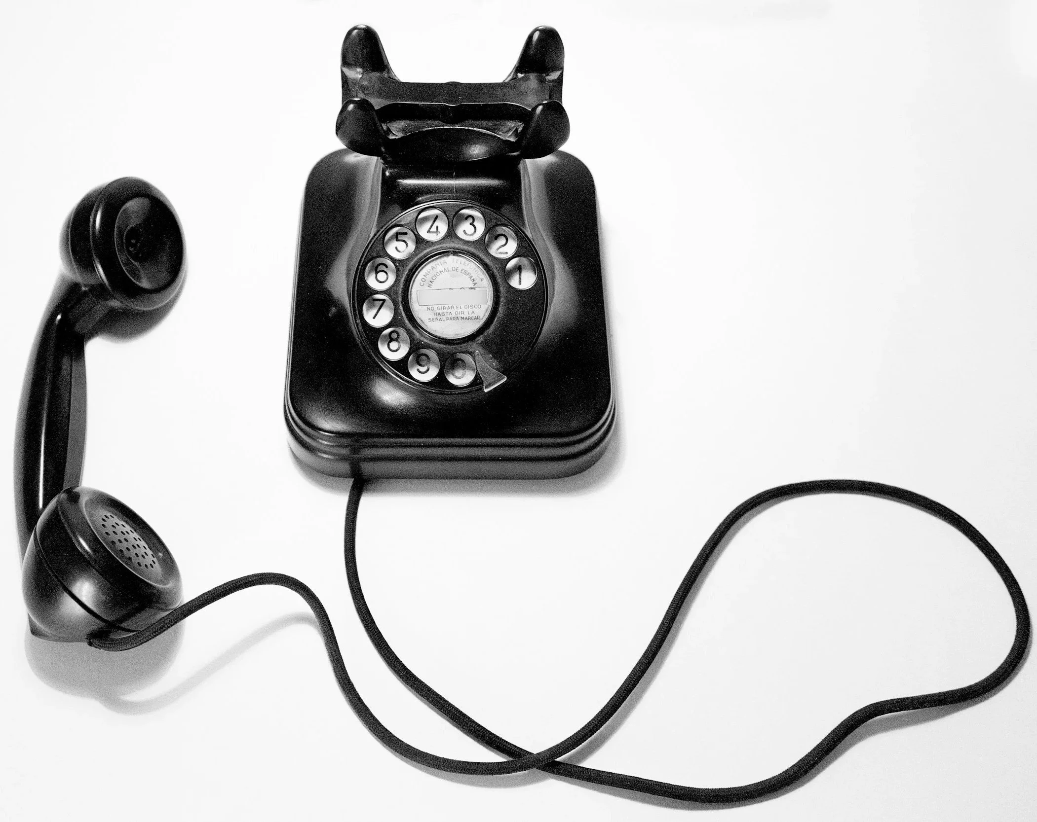 Black rotary dial telephone with cord on white surface.