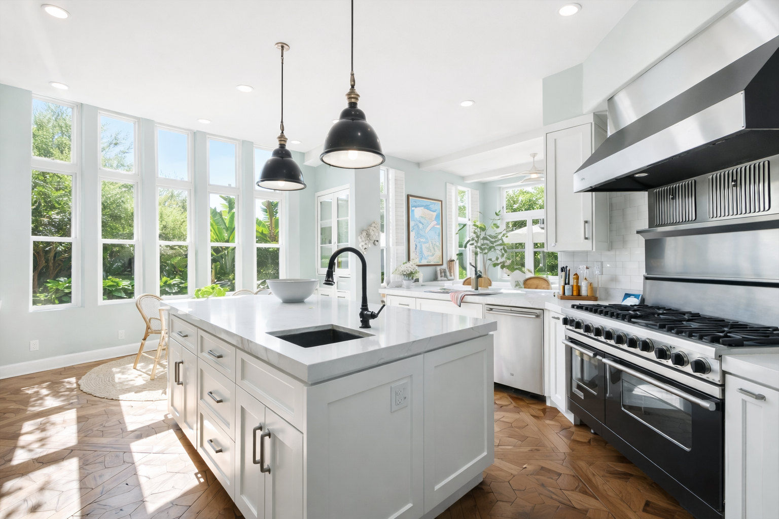 Bright kitchen with large windows, white cabinetry, black appliances, marble island, pendant lights, and wooden flooring.
