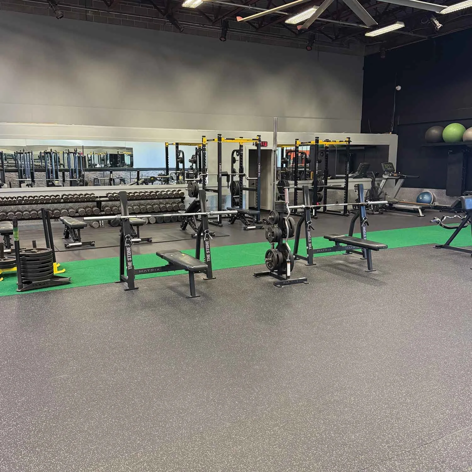 Empty gym with weightlifting equipment, benches, dumbbells, and exercise machines, with a mirror reflecting part of the space.