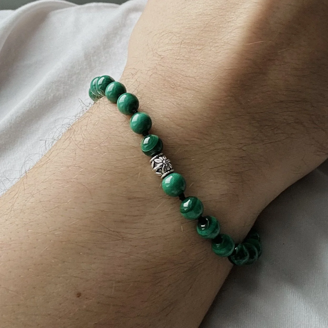 A close-up of a person's wrist wearing a green beaded bracelet with a silver decorative bead in the middle.