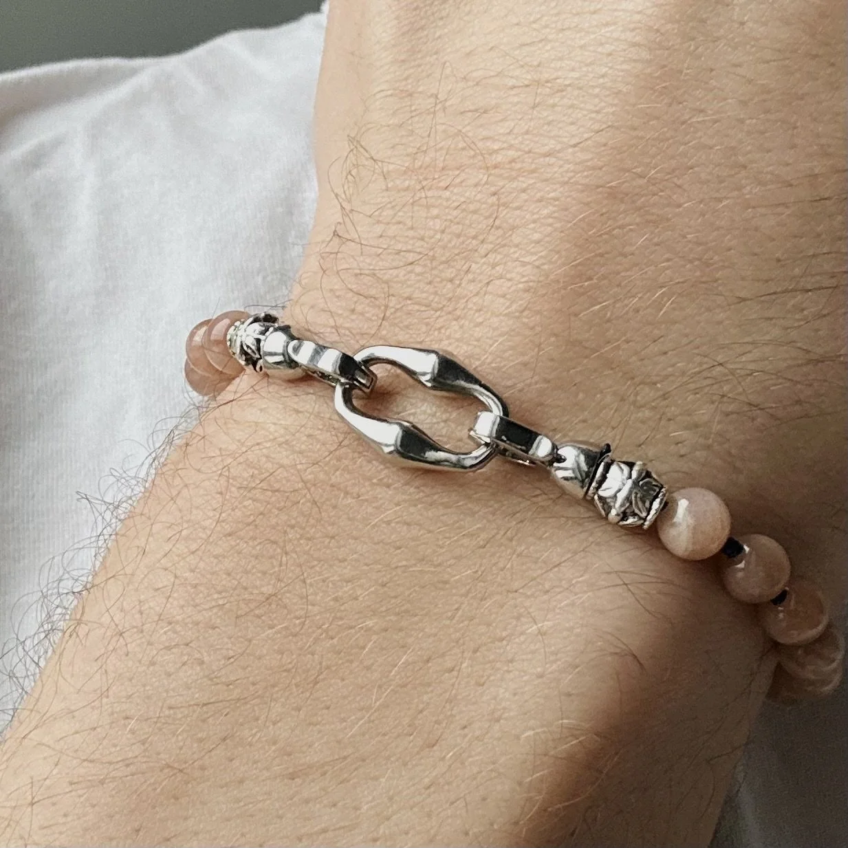 Close-up photo of a person's wrist wearing a silver chain bracelet with various linked and beaded sections.