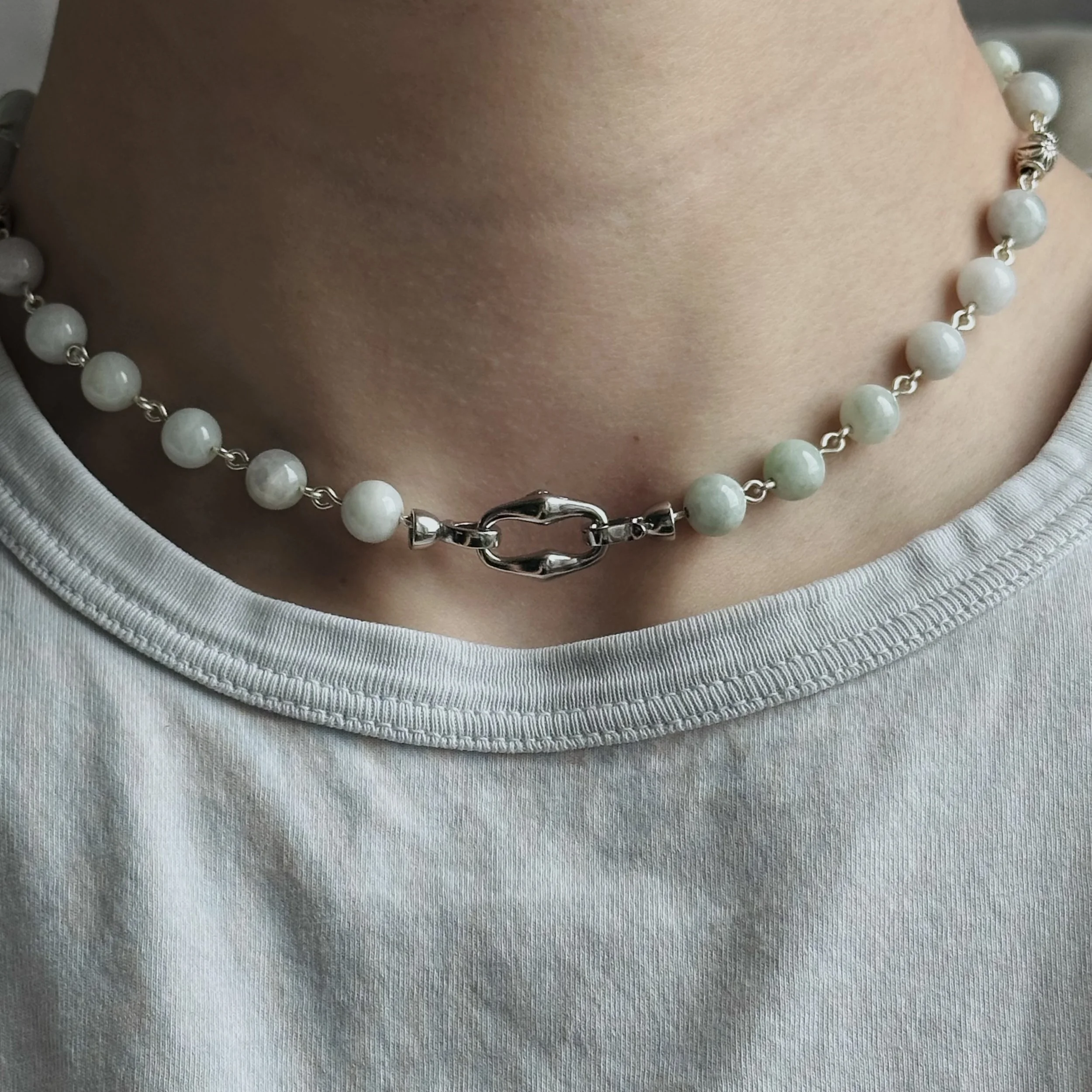 Close-up of a pearl necklace with a silver clasp worn around a person's neck, above a light-colored shirt.