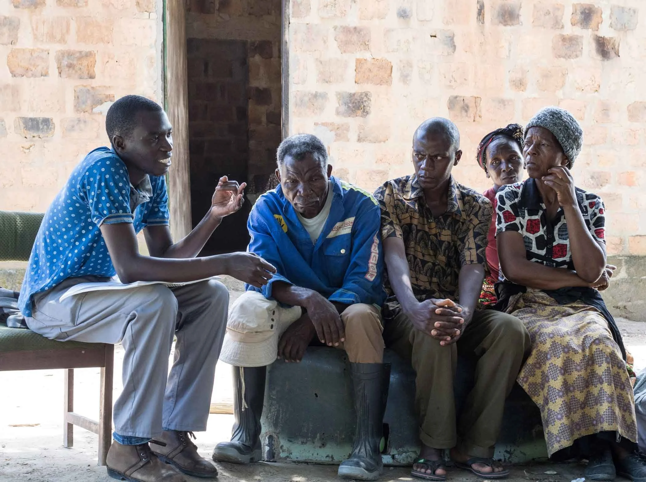 Six people sitting inside a building with exposed brick walls, engaged in a conversation.