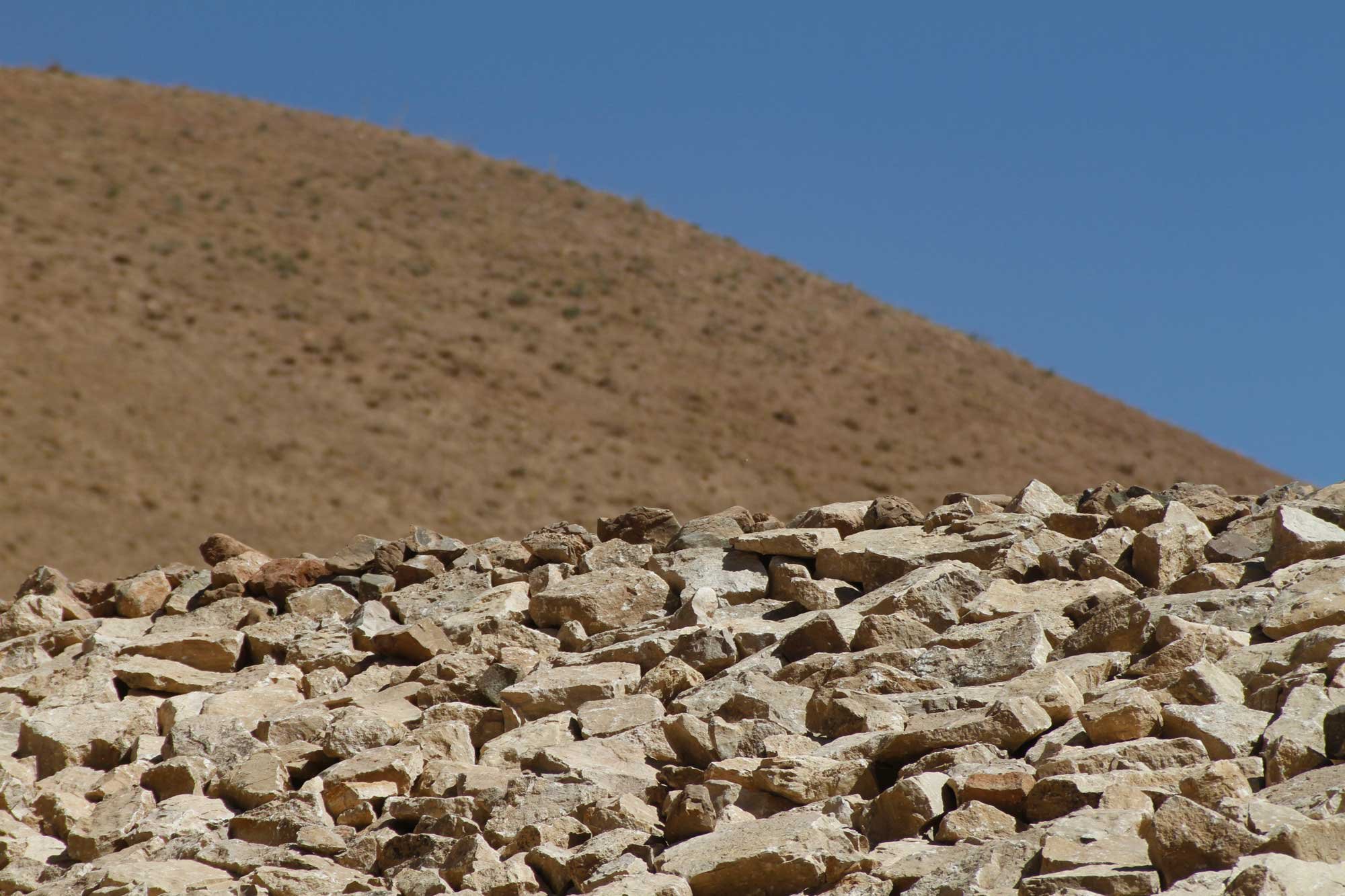 A rocky desert landscape with a brown hillside and a clear blue sky in the background.