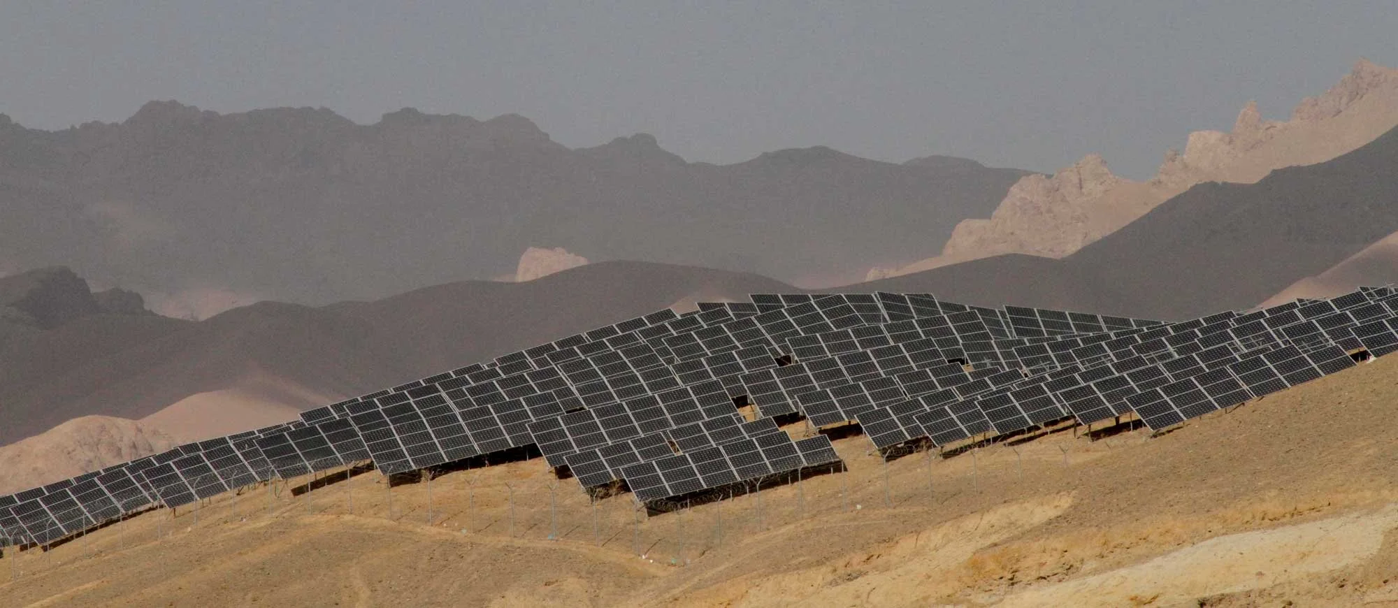 A solar panel array on a hillside in a desert landscape with mountains in the background.