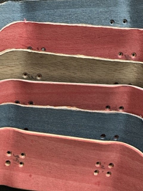Close-up of several skateboard decks stacked together, showing the top surfaces in different colors.
