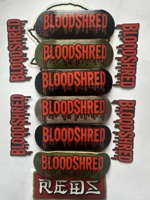 Six fingerboards with the word 'BLOODSHRED' in red letters dripping like blood, on black, green and grey backgrounds. There are 4 'BloodShred' stickers sitting around them in the same red blood dripping font.