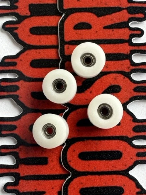 Four white fingerboard skateboard wheels with metal  bearings on a red and black skateboard deck thats says 'BloodShred'.