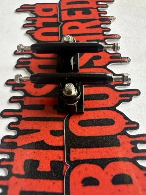 Two skateboard trucks sitting on a 'BloodShred' logo sticker with a red and black graphic design in dripping blood font.